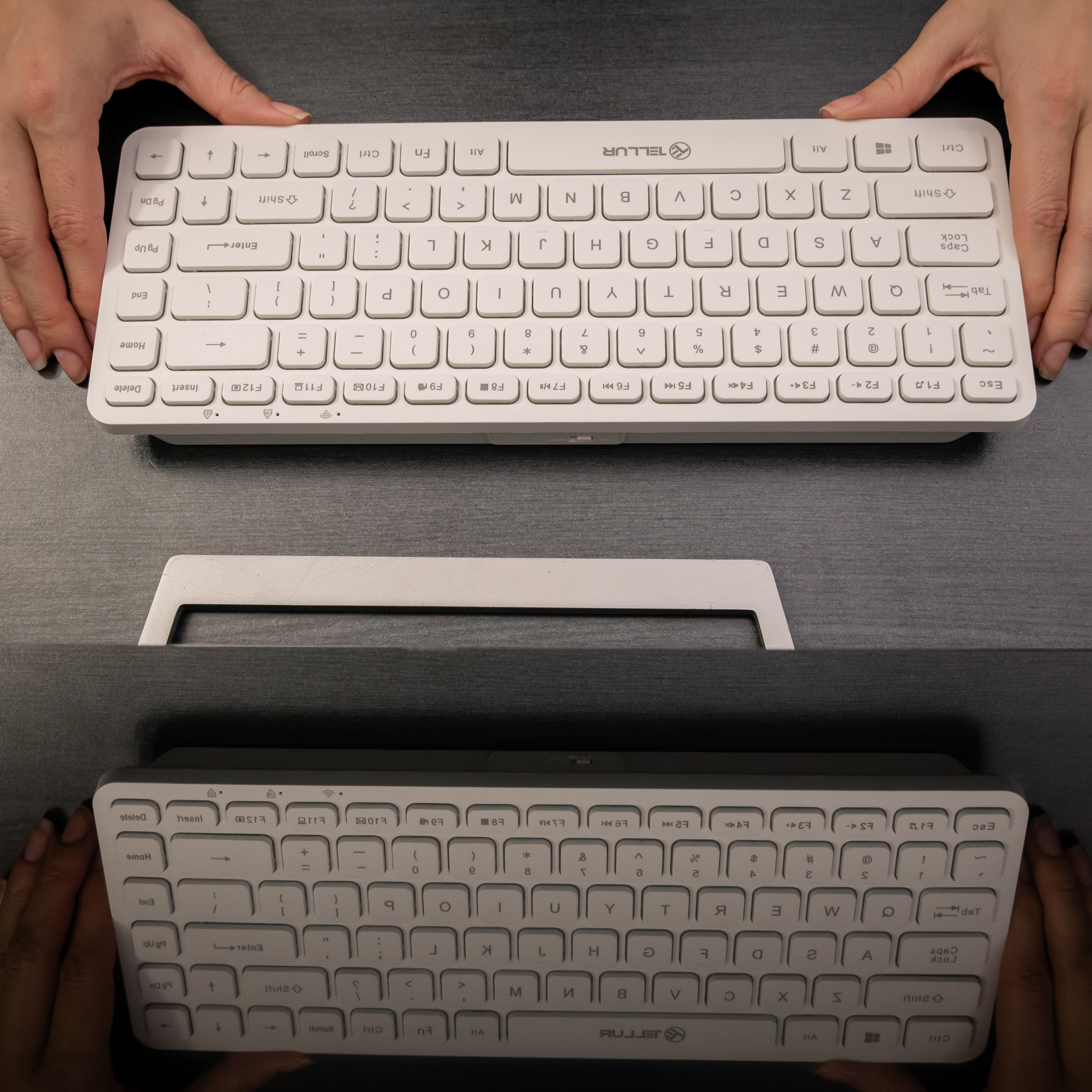 Dłonie trzymające białą klawiaturę. Klawiatura ma białe klawisze z czarnym tekstem. Na ciemnej powierzchni.