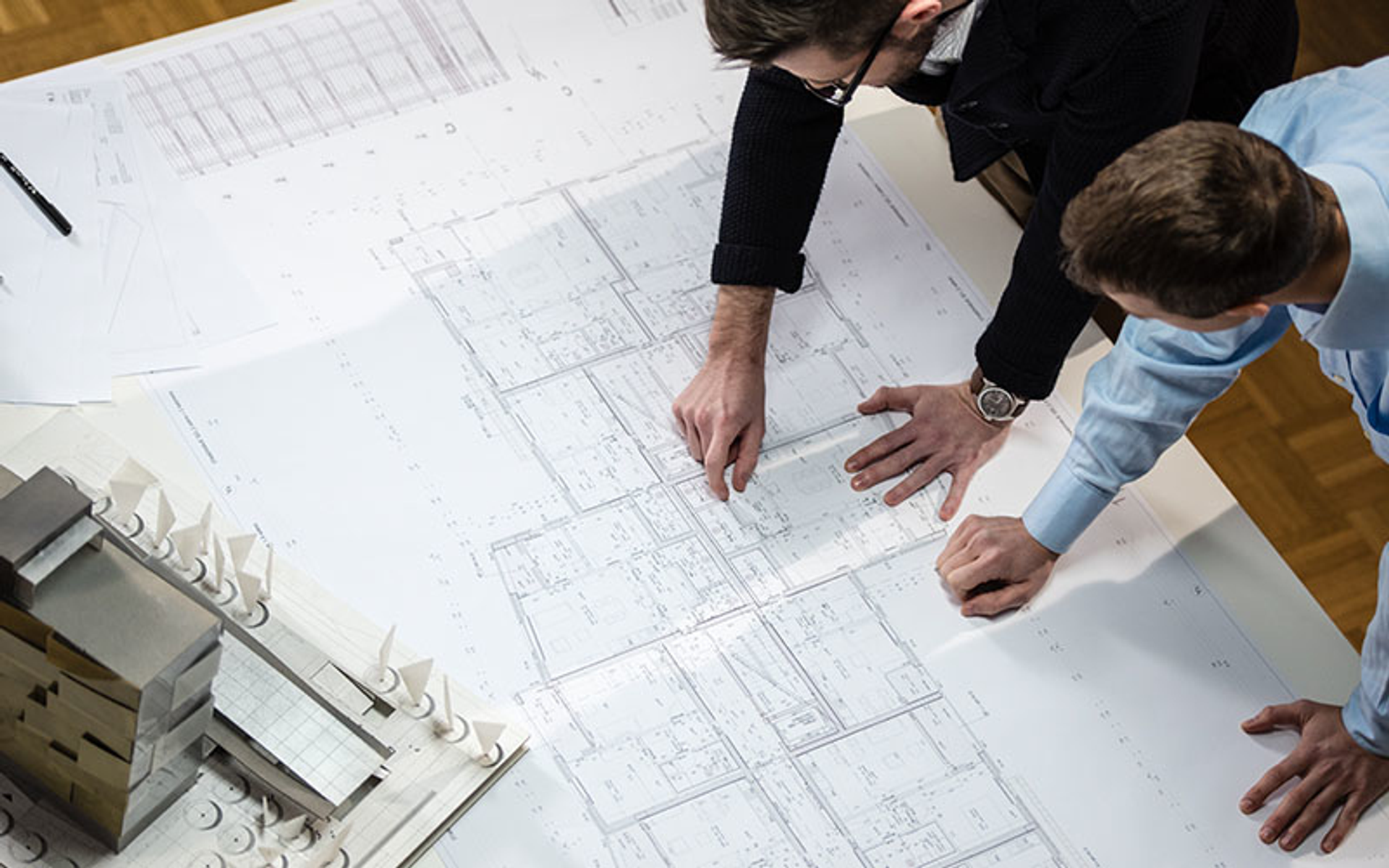 Dwóch mężczyzn oglądających plany i model. Widok z góry na stół z planami i modelem.