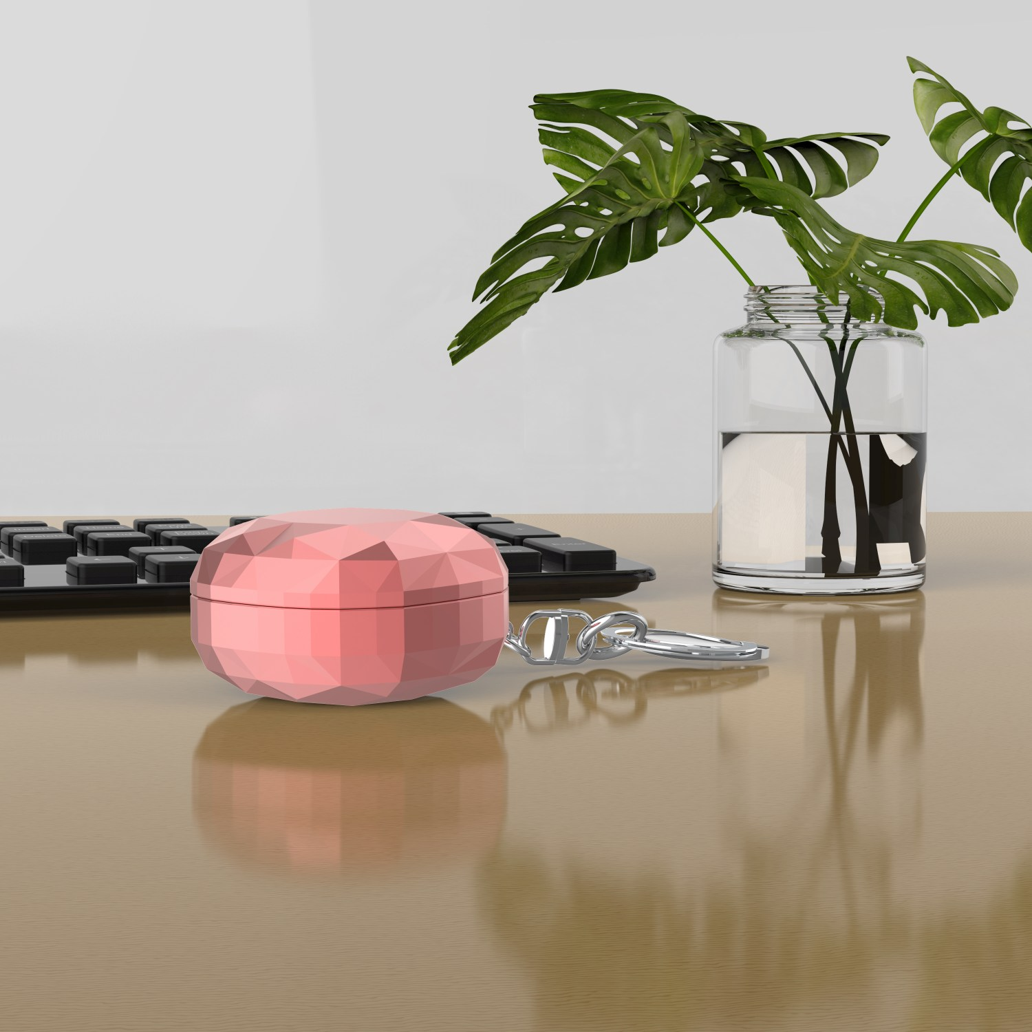 Rosa geometrische Ohrhörerhülle mit Schlüsselanhänger, auf Tisch mit Tastatur und Pflanze.