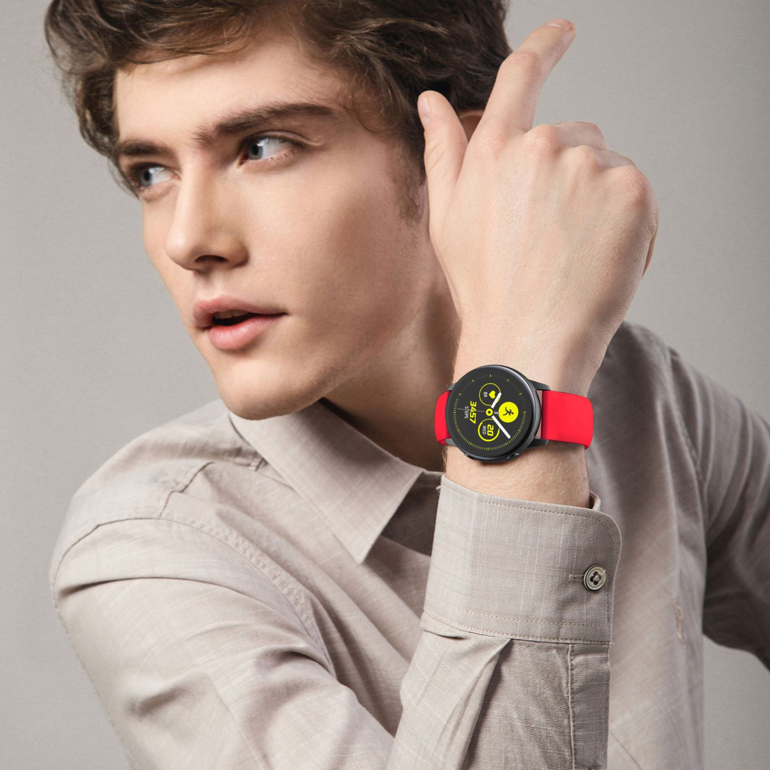 Mann trägt Hemd, rote Smartwatch am Handgelenk, zeigt nach oben. Heller Hintergrund.