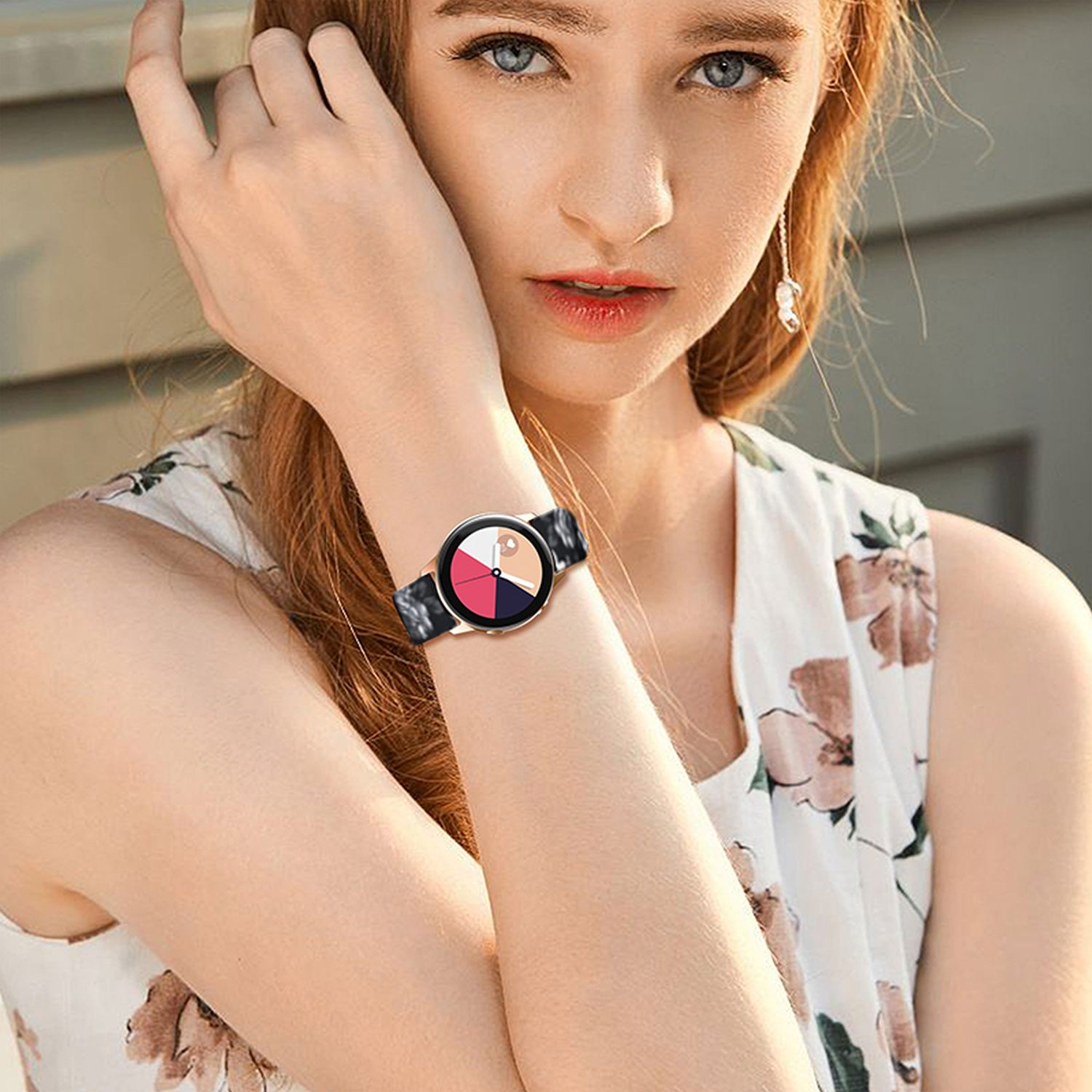 Das Handgelenk einer Frau mit einer Uhr. Die Uhr ist schwarz mit einem farbigen Zifferblatt. Das Armband ist ebenfalls schwarz.