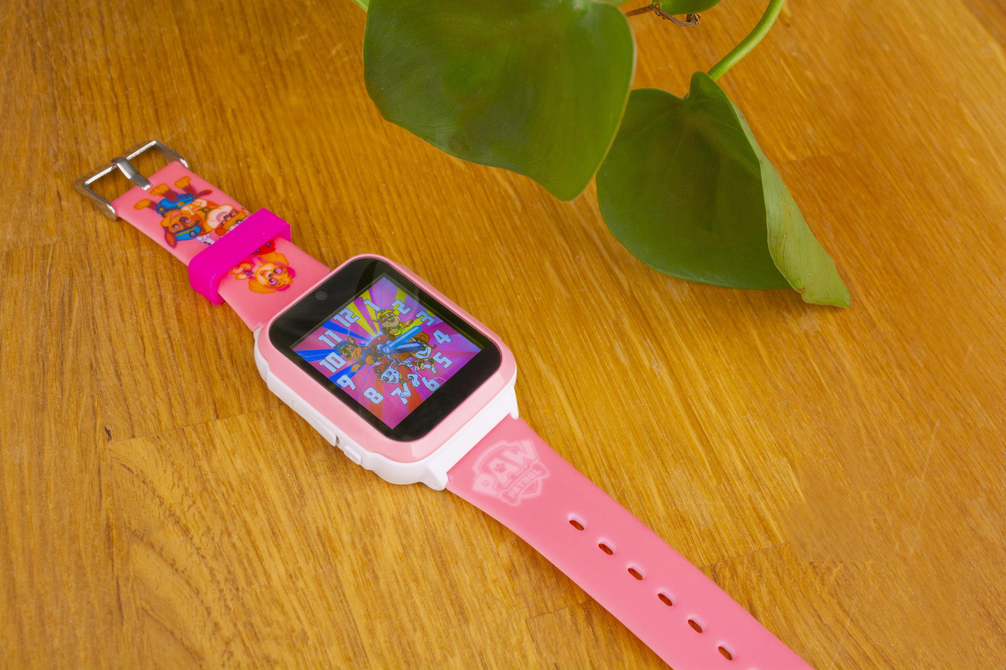 Smartwatch rosa Paw Patrol su tavolo di legno con sfondo di foglie verdi.