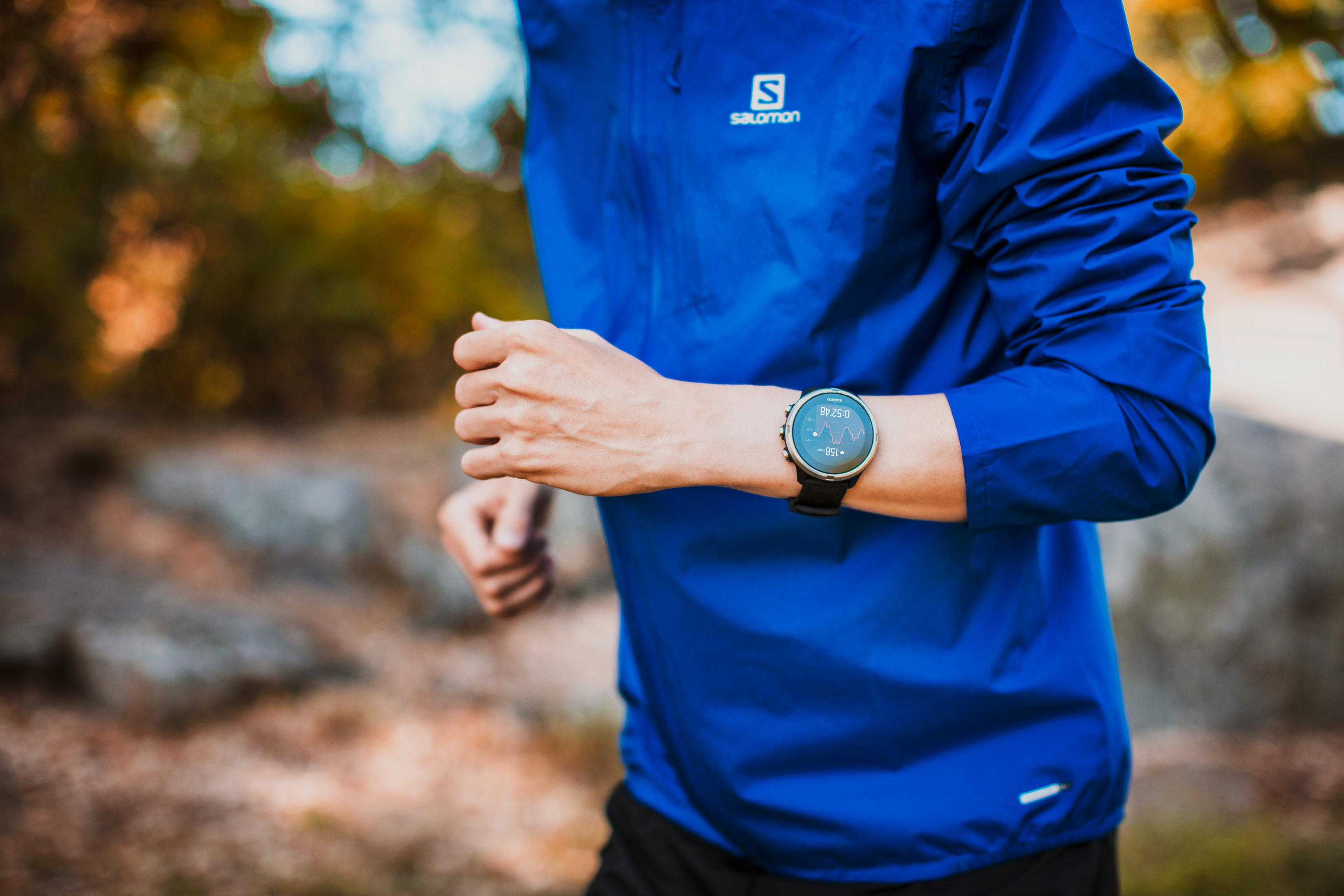 Eine Person, die mit einer Smartwatch am Handgelenk rennt. Der Hintergrund sind verschwommene Bäume und Laub.