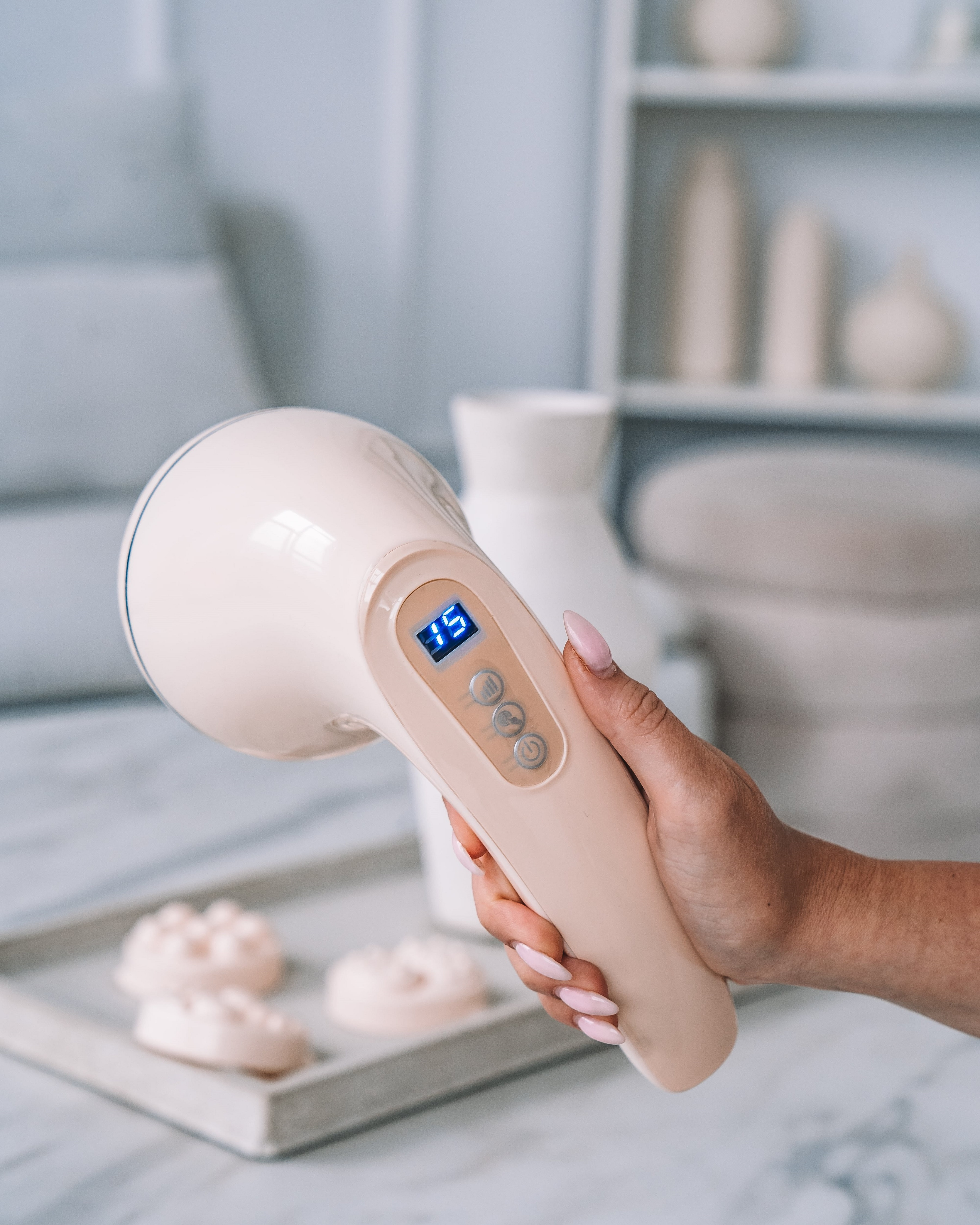 Eine Hand hält ein Massagegerät. Das Gerät ist beige mit einer Digitalanzeige, die die Zahl 15 zeigt.