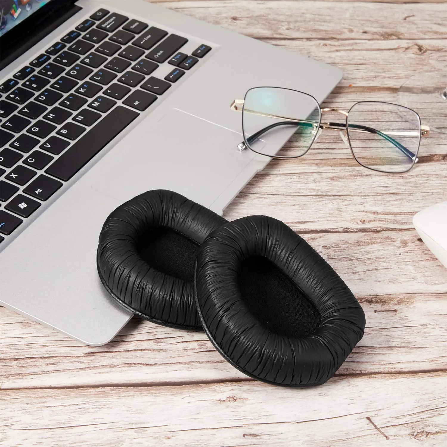 Na klawiaturze laptopa leżą poduszki słuchawkowe i okulary na drewnianym stole.