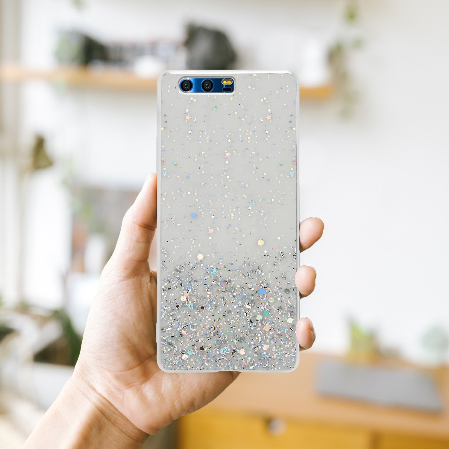 Eine Hand, die ein Telefon mit einer durchsichtigen Glitzerhülle hält und ein dekoratives Design zeigt.