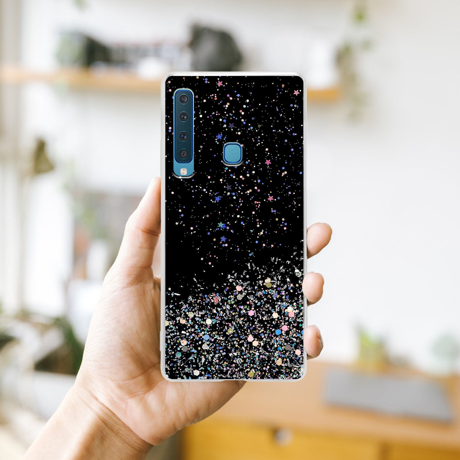 Una mano che tiene una custodia per telefono con un design glitterato nero. La custodia ha un design colorato.