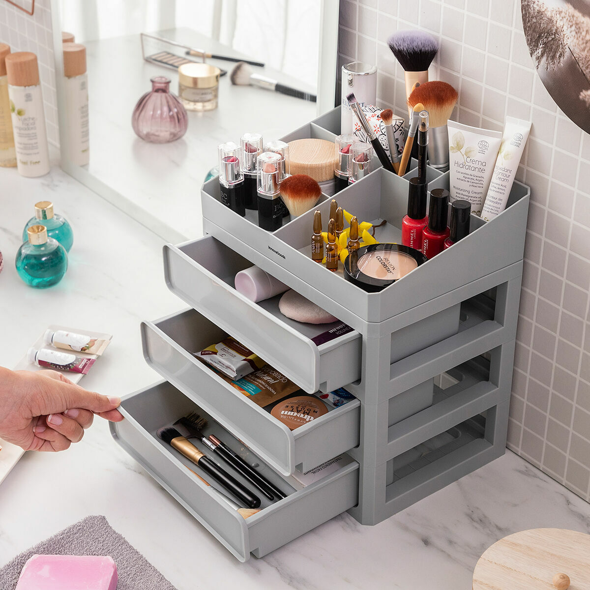 Grauer Make-up-Organizer mit Schubladen. Kosmetika im Inneren. Hand öffnet eine Schublade. Weißer Hintergrund.