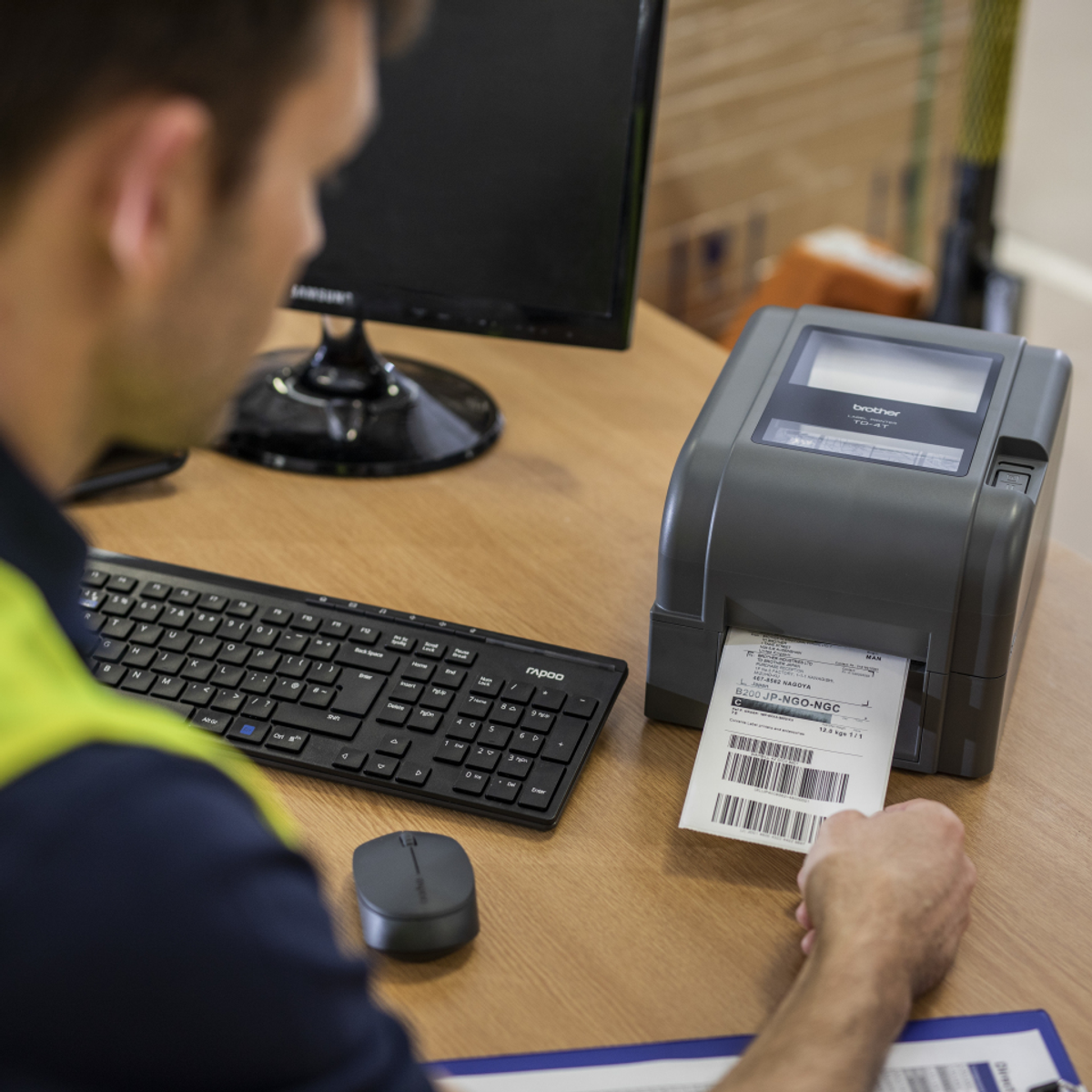 Mężczyzna używający drukarki etykiet. Etykieta jest drukowana, obecny jest komputer i klawiatura.