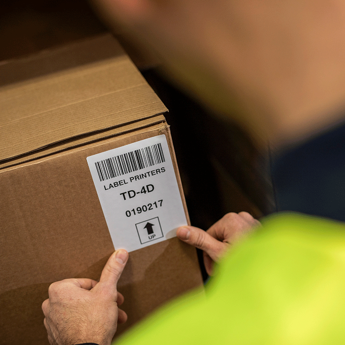 Hand einer Person, die auf ein Etikett auf einem Karton mit Barcode und Text zeigt.