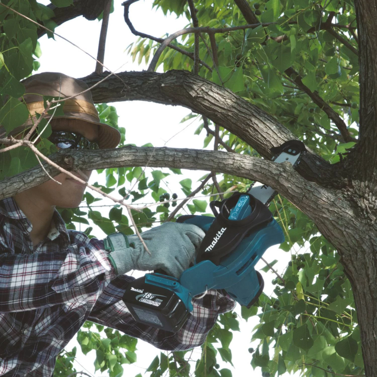 Mężczyzna używa piły łańcuchowej Makita do cięcia gałęzi drzewa. Nosi rękawice i okulary ochronne.
