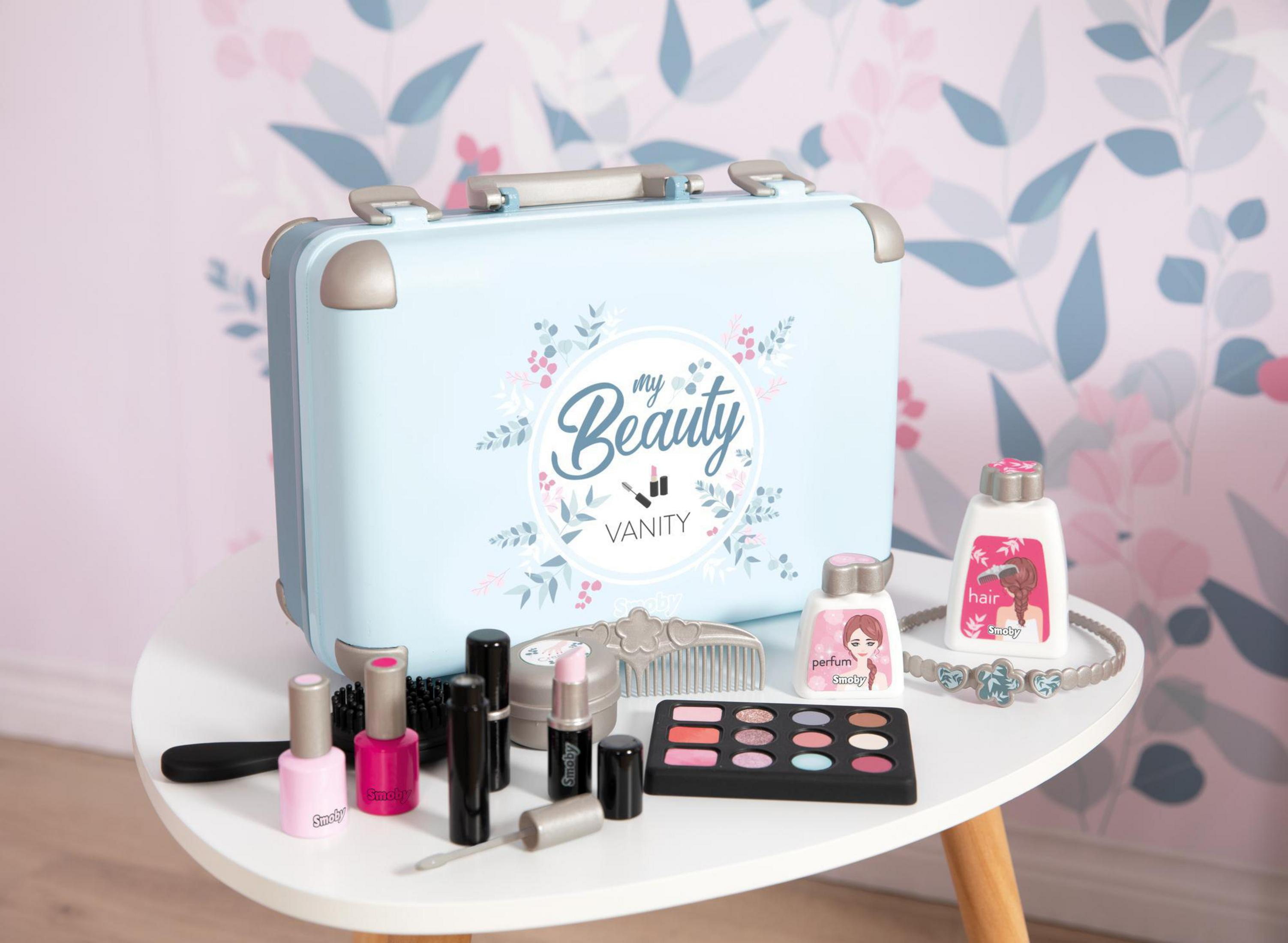 Eine blaue Spielzeug-Kommode mit Make-up-Zubehör auf einem weißen Tisch. Ein rosa Blumenhintergrund.