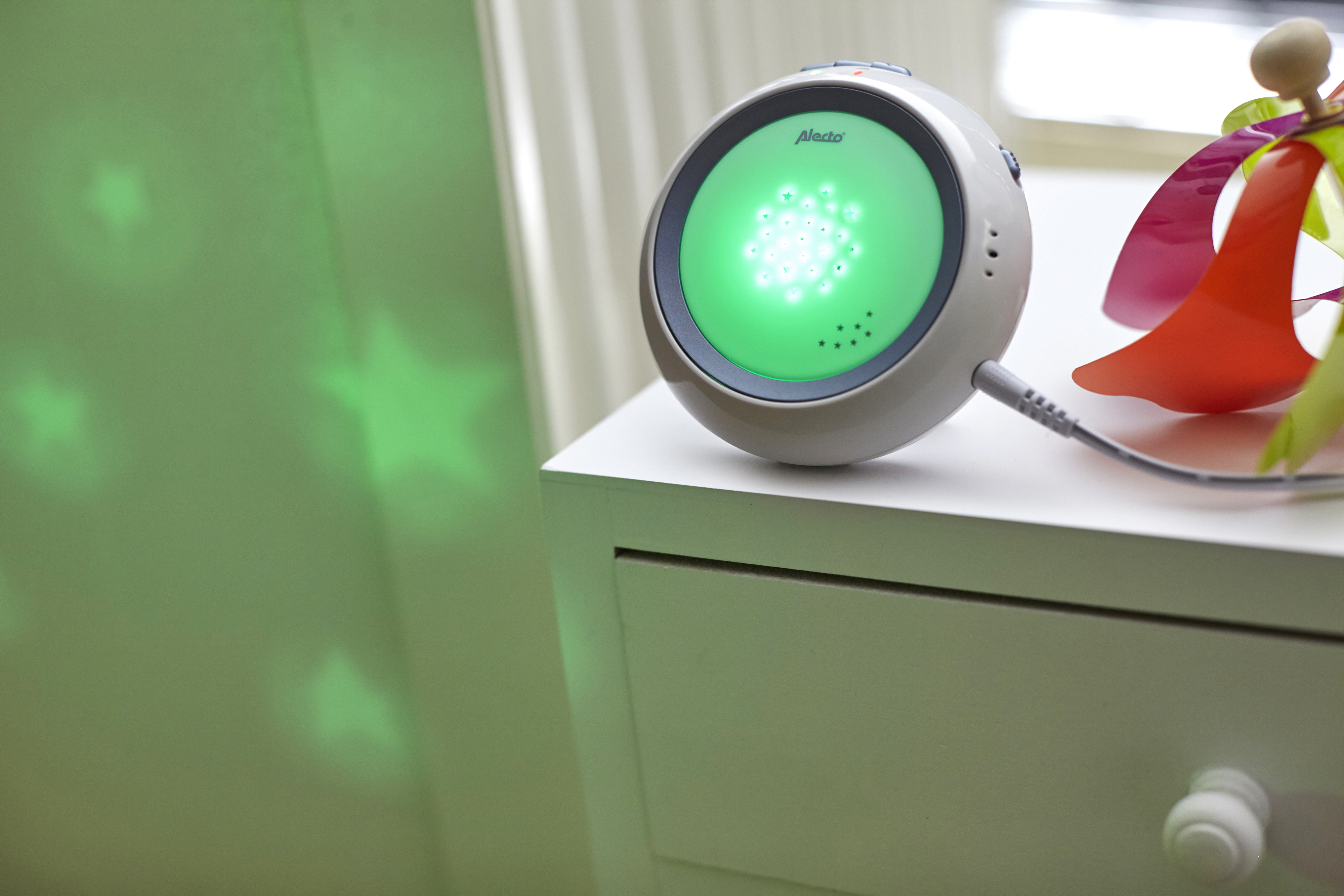 Een babyfoon op een witte commode. Het projecteert groene sterren op de muur.