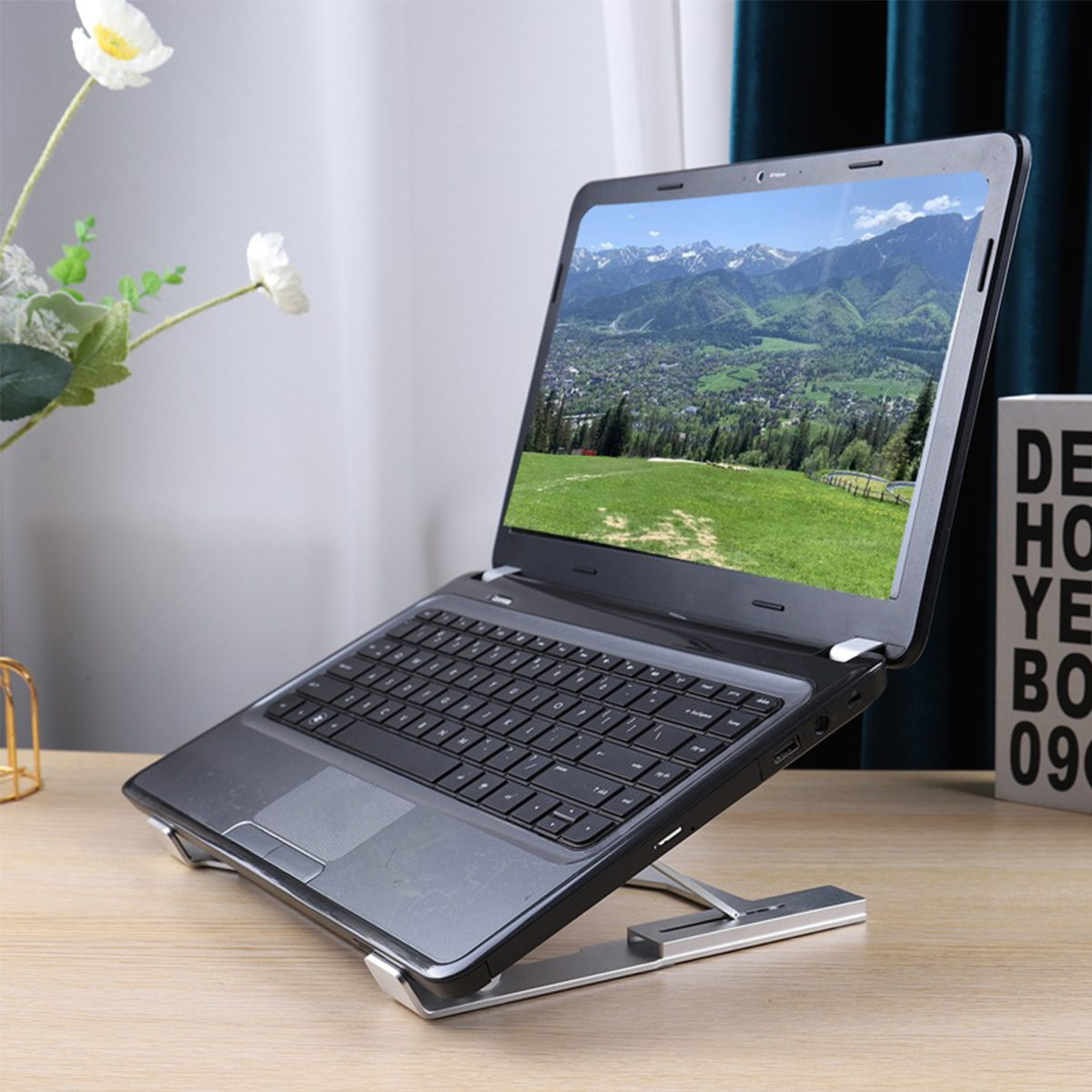 Laptop auf silbernem Ständer, Bildschirm zeigt Berglandschaft.