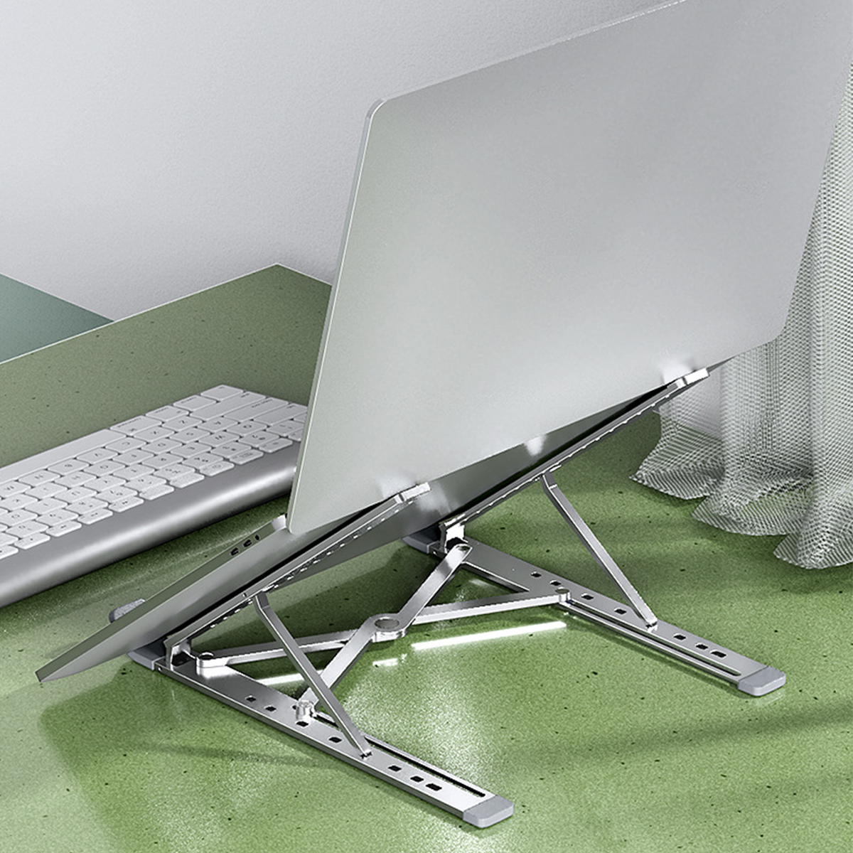 Ein silberner Laptop auf einem silbernen, verstellbaren Ständer, auf einem grünen Schreibtisch.