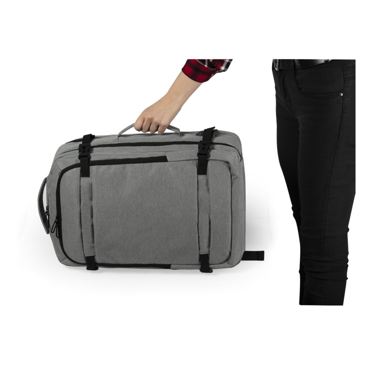 Una persona sostiene una bolsa de viaje gris. La bolsa es rectangular, con correas y hebillas negras. La persona usa pantalones negros.