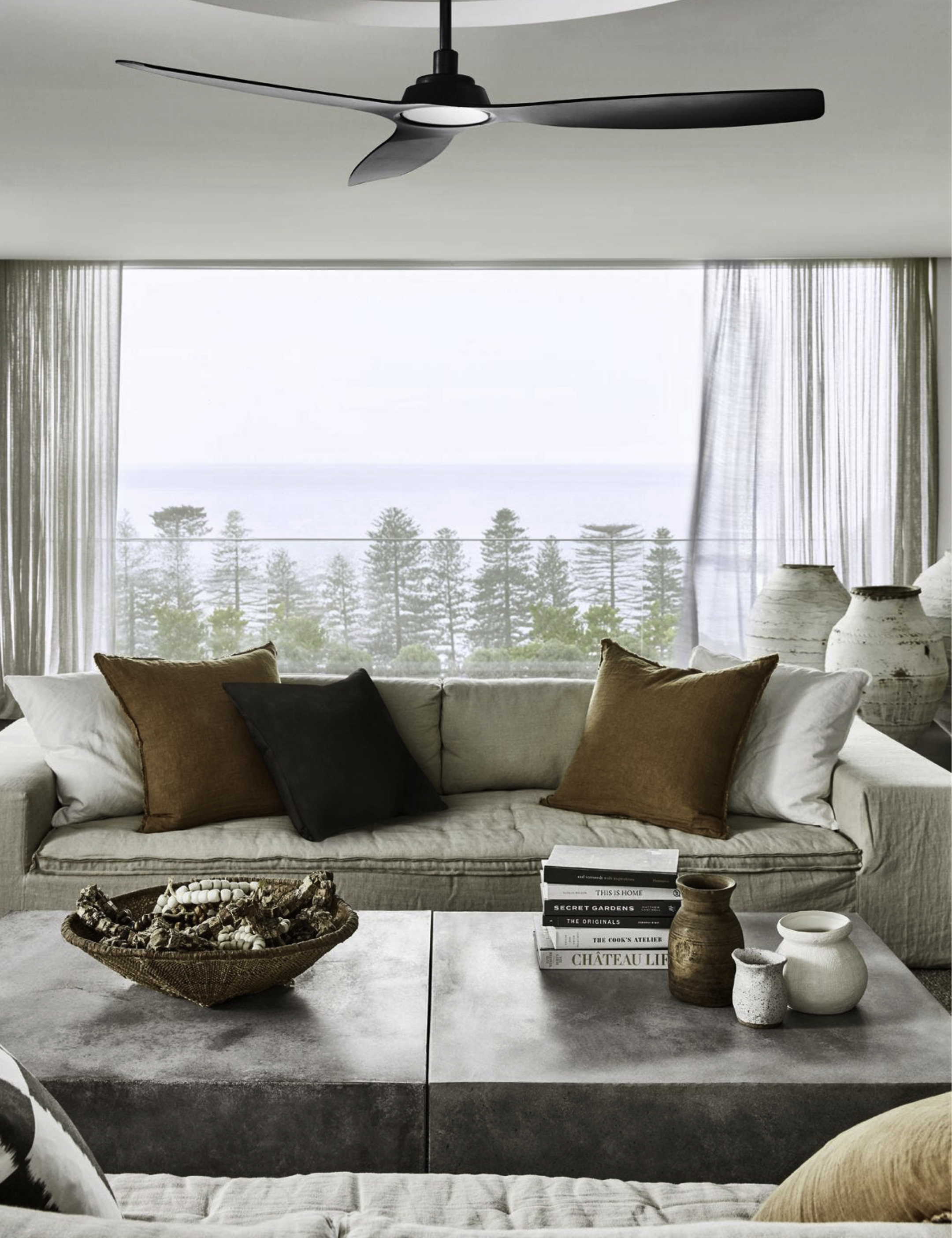 Ein Wohnzimmer mit Deckenventilator, Sofa, Kissen und Dekoration. Es hat ein großes Fenster mit Landschaftsblick.