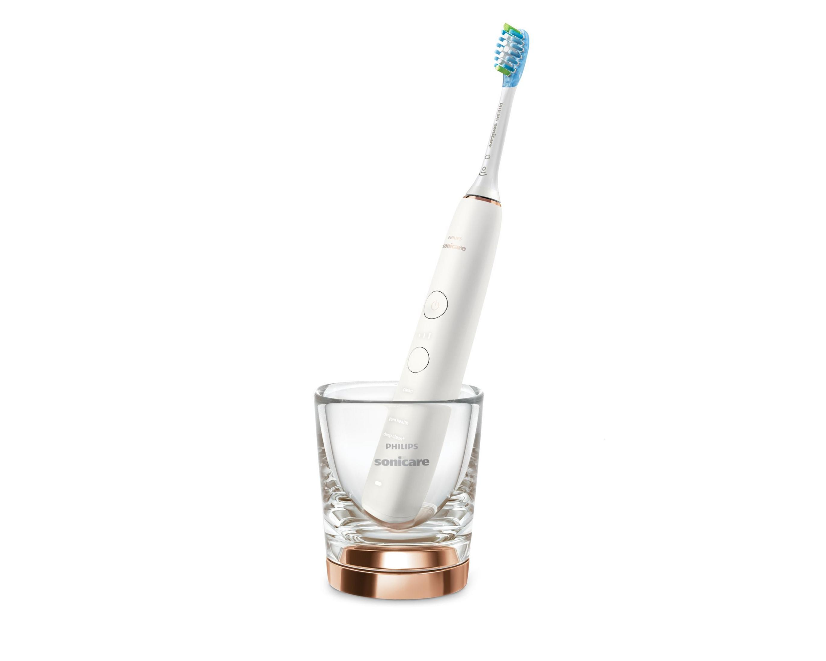 Een elektrische tandenborstel in een helder glas en een roségouden voet, geïsoleerd op een witte achtergrond.