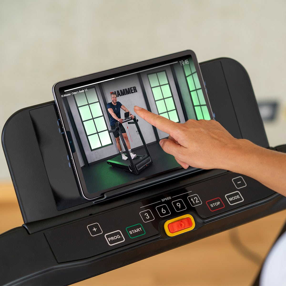 Eine Person benutzt ein Tablet auf einem Laufband, um sich ein Trainingsvideo anzusehen.