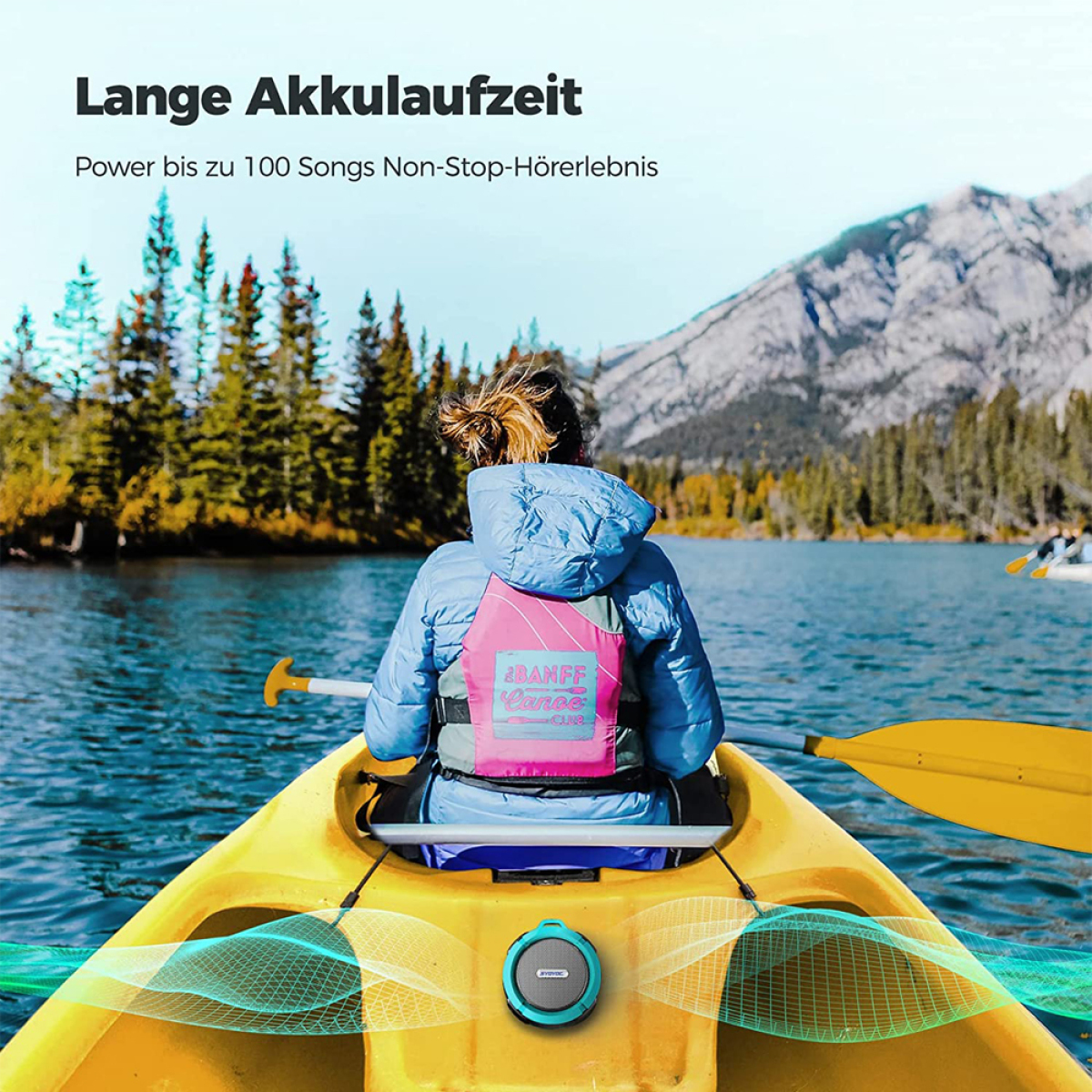Eine Frau in einem Kajak auf einem See. Sie trägt eine Schwimmweste. Berge und Bäume im Hintergrund.