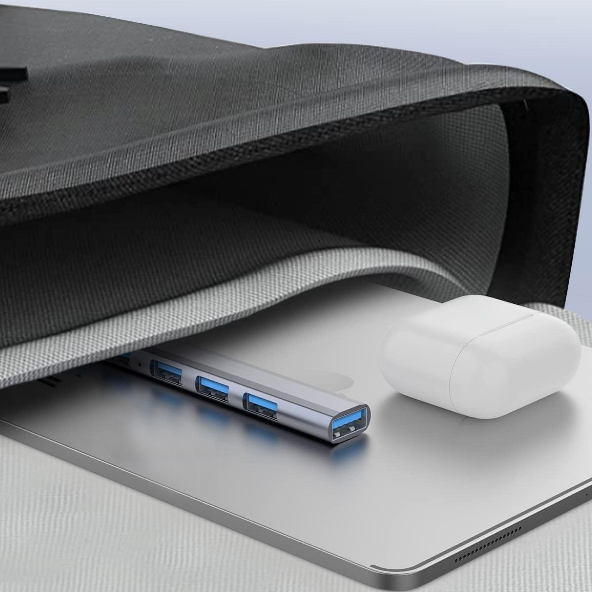 Laptop, USB-Hub und AirPods in einer Tasche. Silberner Hub mit blauen Anschlüssen. Weiße AirPods.