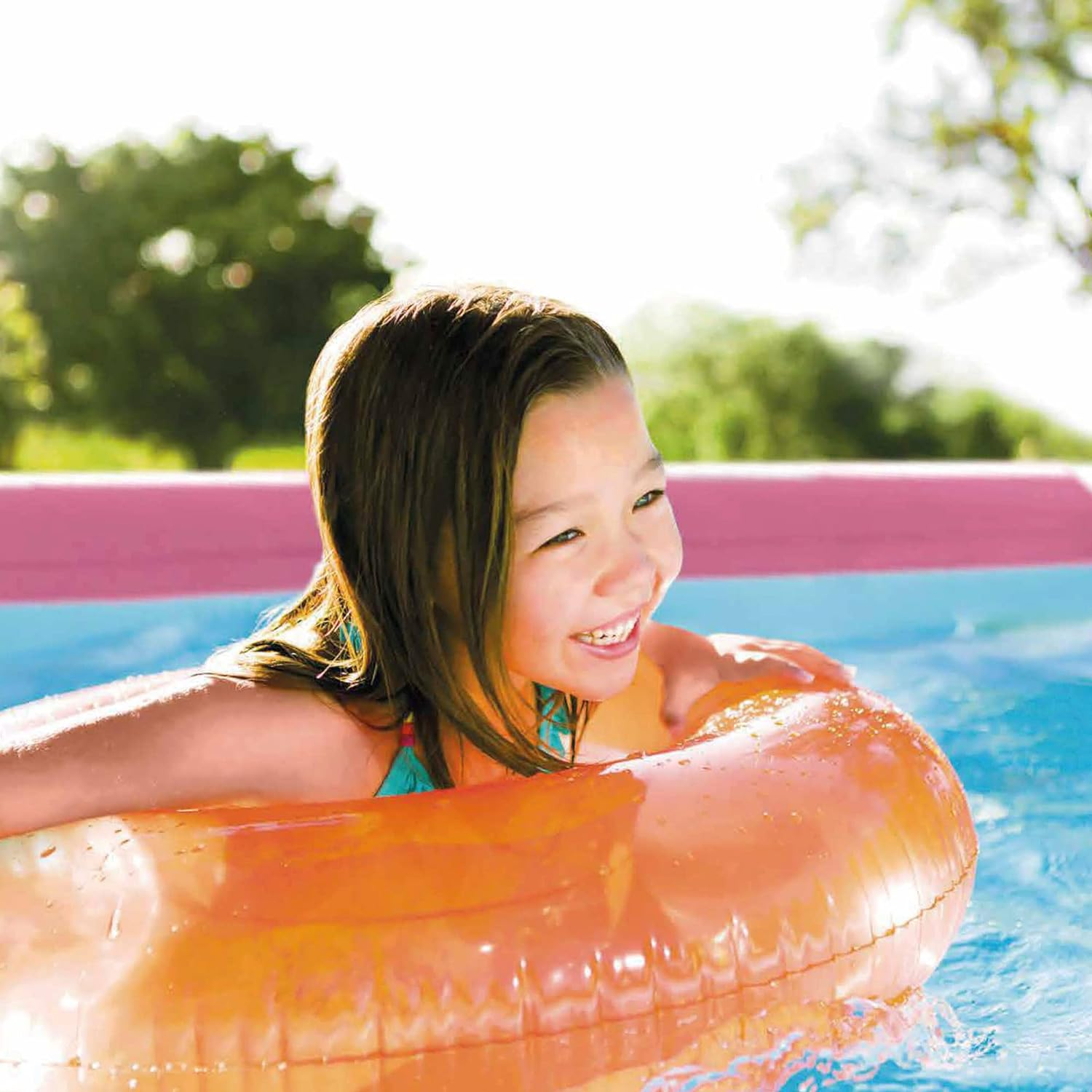 Junges Mädchen in einem orangefarbenen Schwimmring in einem Schwimmbecken. Lächelt in die Kamera.