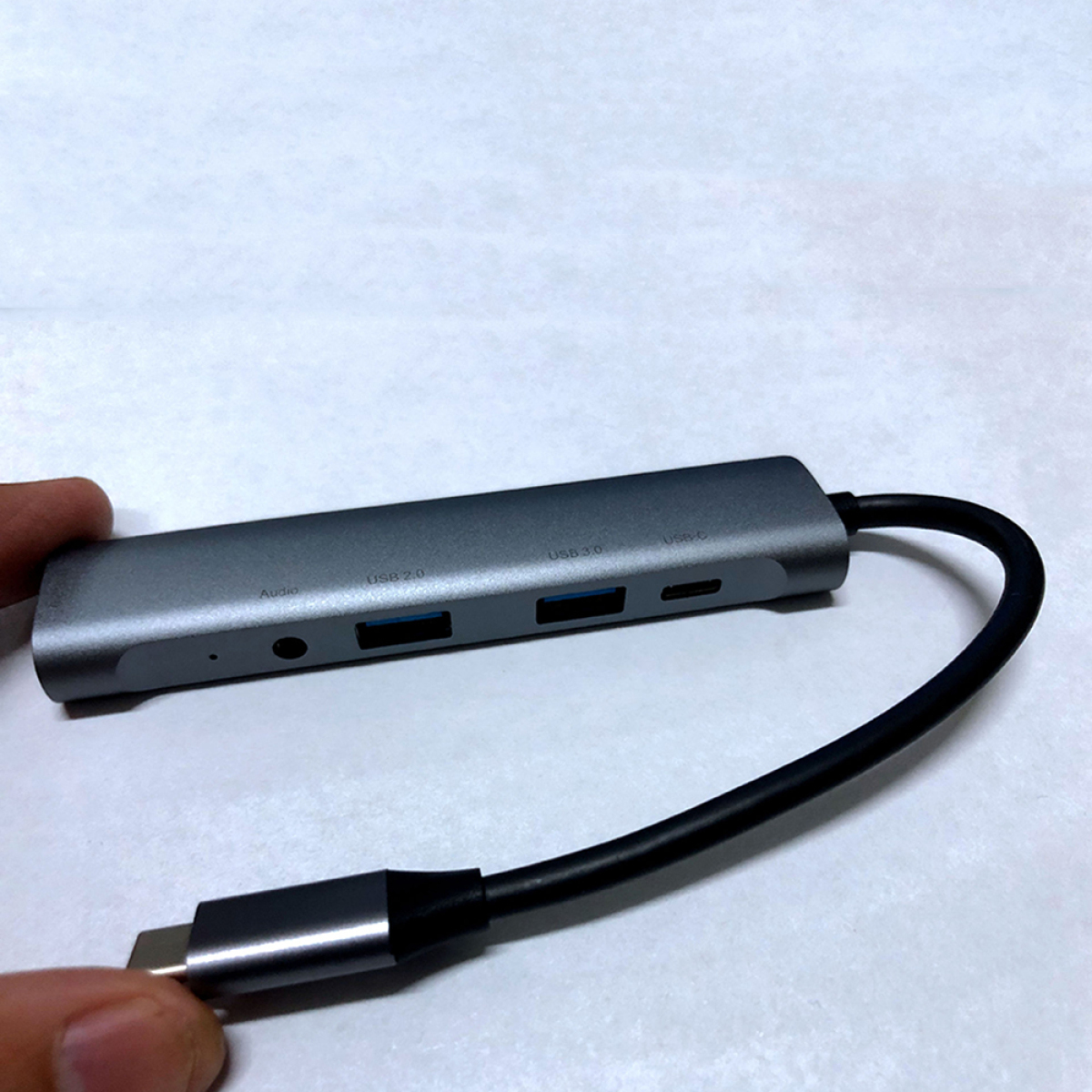 Silberner USB-Hub mit USB 2.0-, 3.0- und USB-C-Anschlüssen. Schwarzes Kabel angeschlossen, Hand hält.