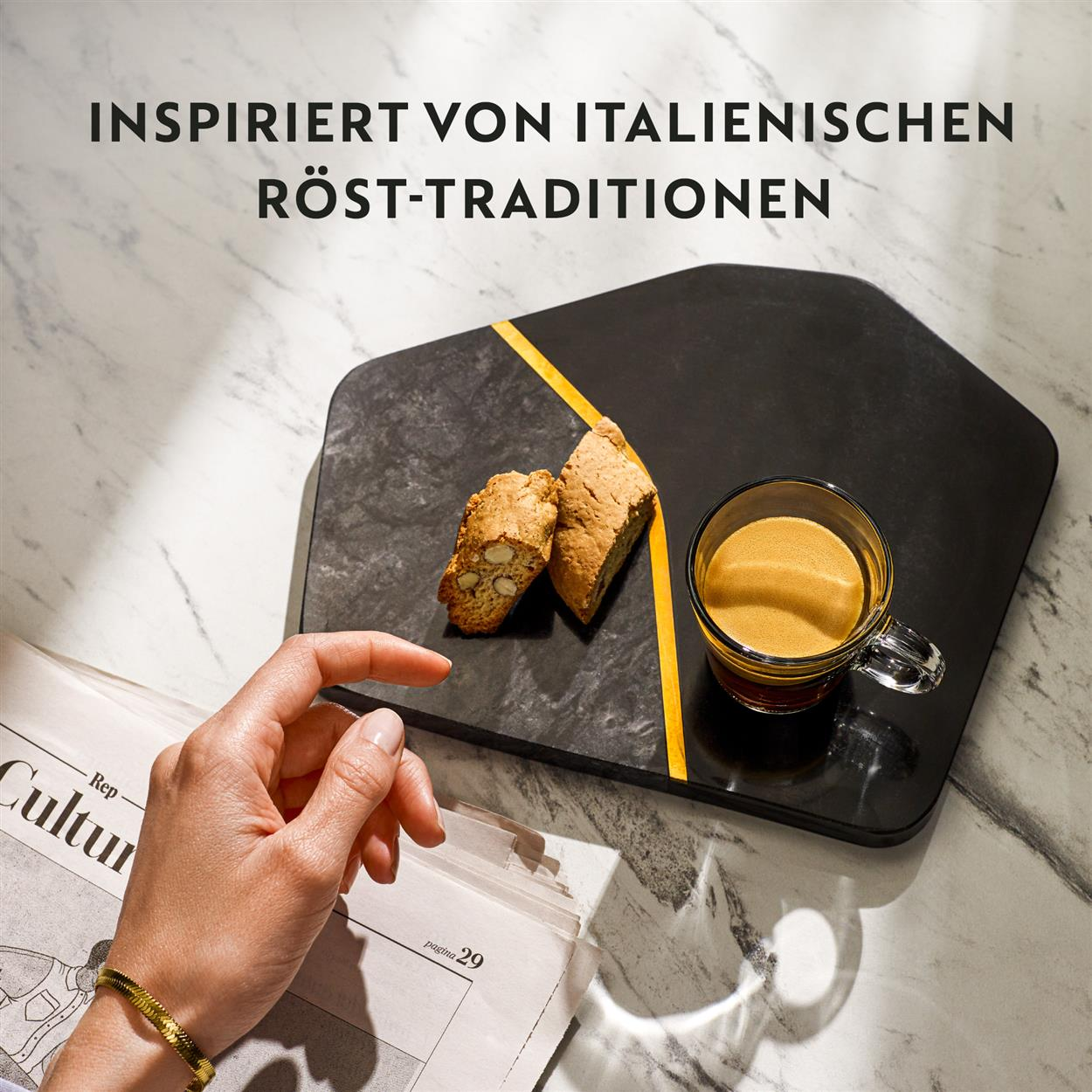 Hand hält Biscotti und eine Tasse Kaffee mit einer Zeitung. Schwarzes Servierbrett mit gelbem Streifen.