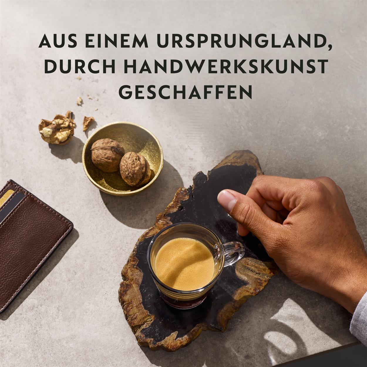 Eine Hand greift nach einer Tasse Kaffee auf einer Holzoberfläche. Walnüsse und eine Geldbörse sind in der Nähe. Text ist oben.
