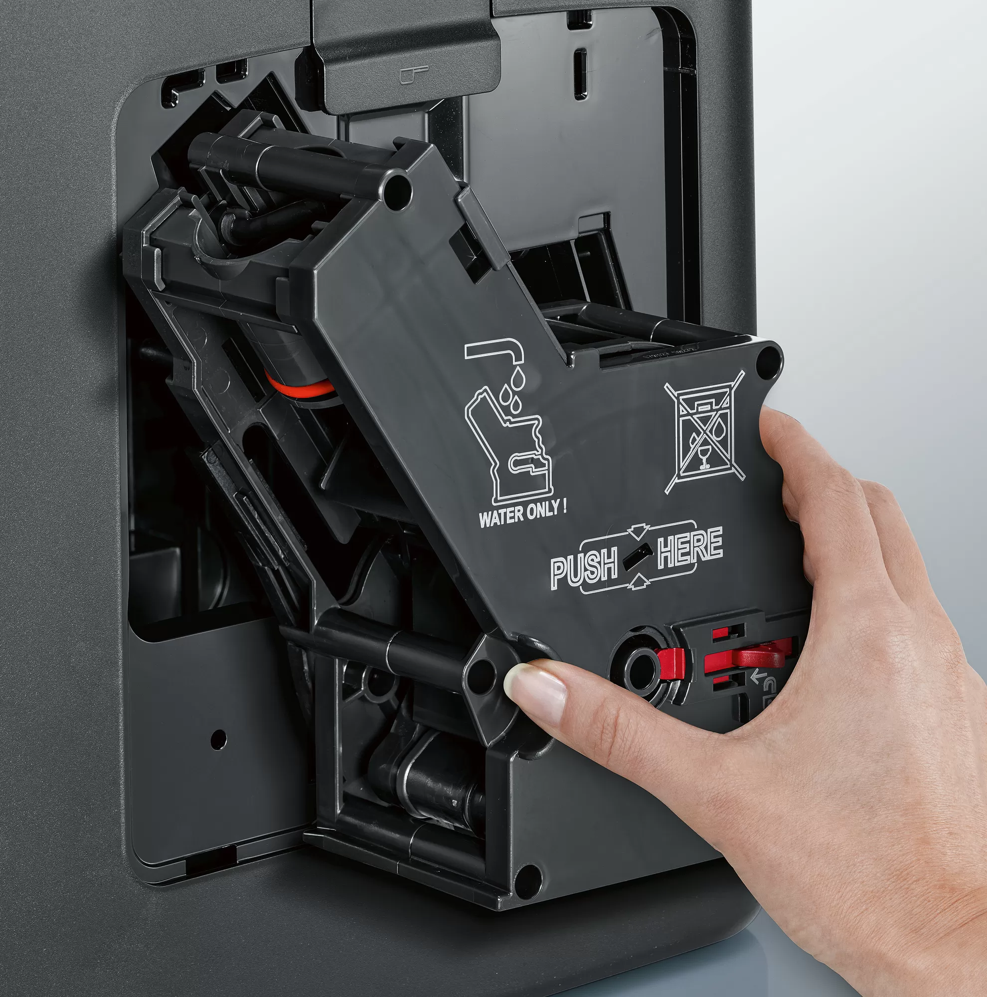 Ręka otwiera element ekspresu do kawy. Pokazuje wewnętrzny mechanizm maszyny.