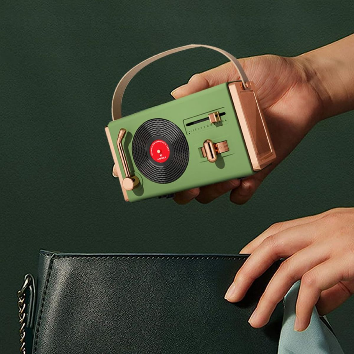 Eine Person hält einen grünen Retro-Plattenspieler und legt ihn in eine schwarze Handtasche. Goldener Griff.