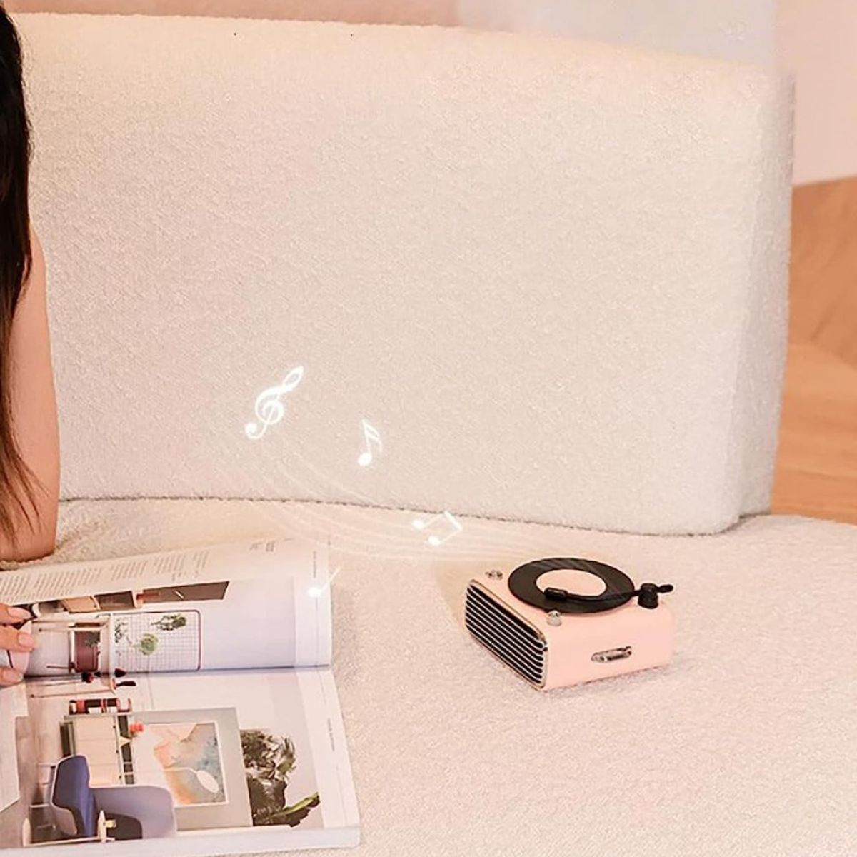 Ein rosa Plattenspieler im Retro-Stil mit darüber schwebenden Noten. Ein Magazin ist geöffnet, und eine weiße Couch ist im Hintergrund.