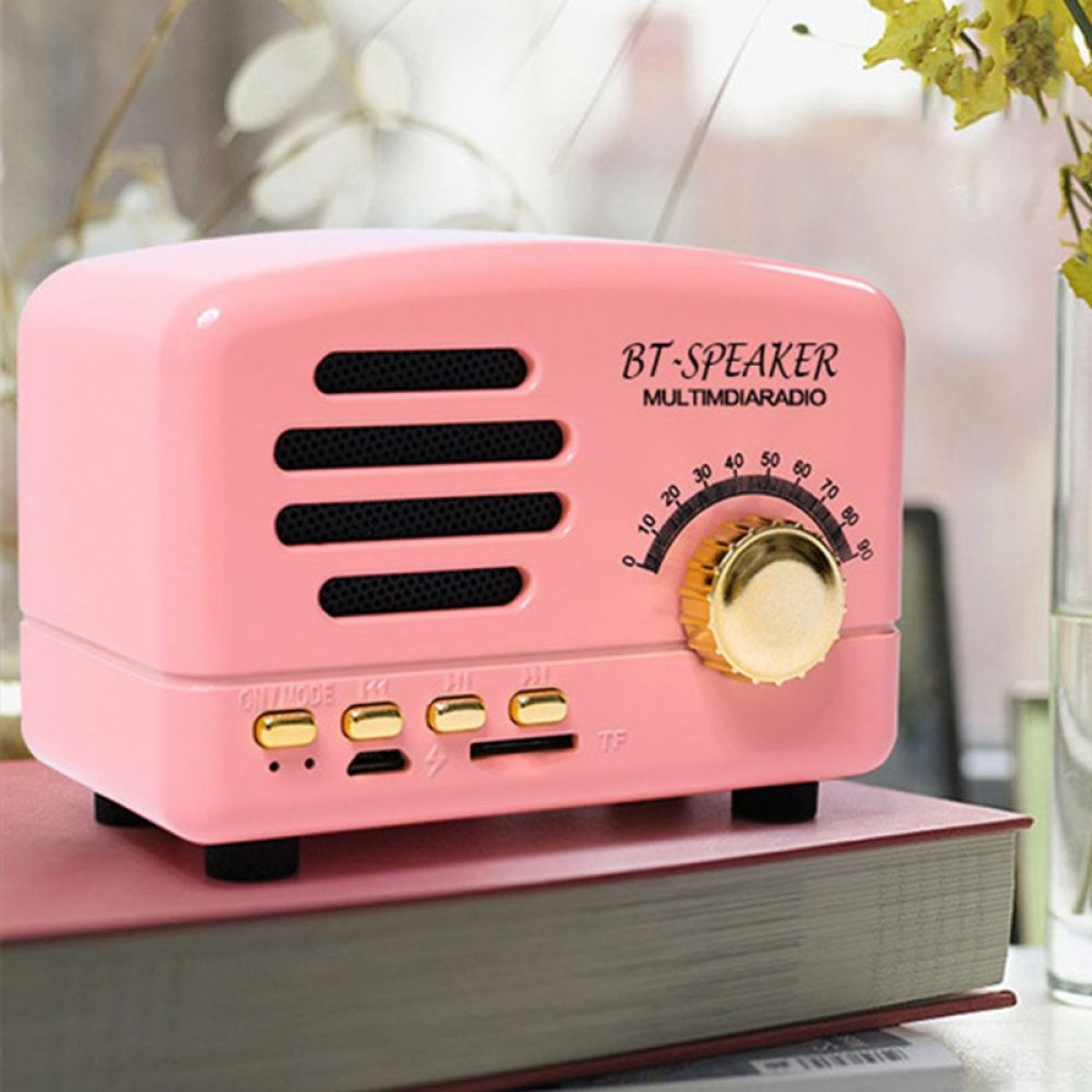 Ein pinkfarbener Lautsprecher im Retro-Stil mit Drehregler und Knöpfen liegt auf einem Buch.