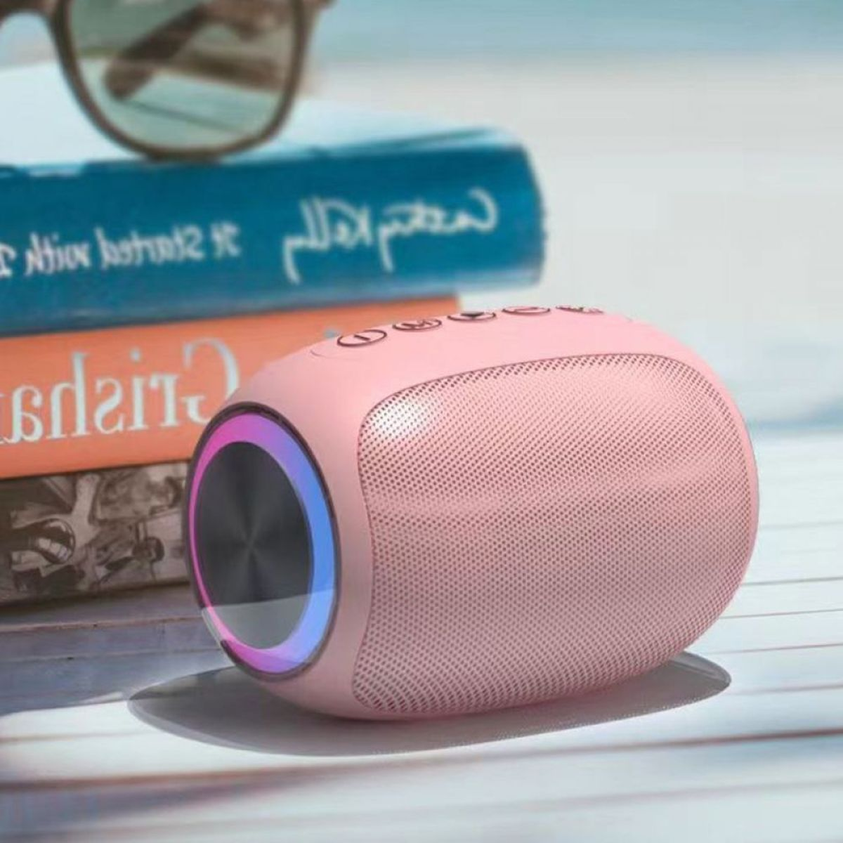 Rosa Lautsprecher mit Knöpfen, Lichtring, Bücher und Sonnenbrille im Hintergrund.
