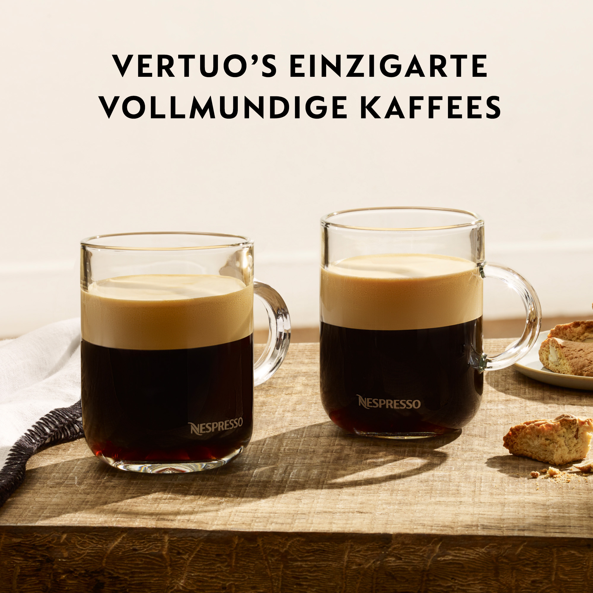 Zwei Glaskrüge Kaffee mit Crema auf einer Holzoberfläche. Text: Vertuo's vollmundige Kaffees.