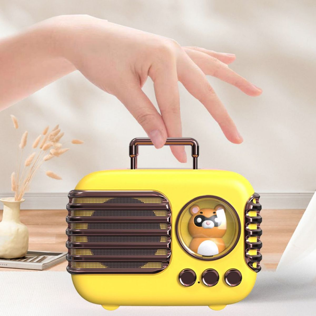 Gelber Lautsprecher im Retro-Stil mit Hamsterfigur. Griff oben, Hand greift danach.