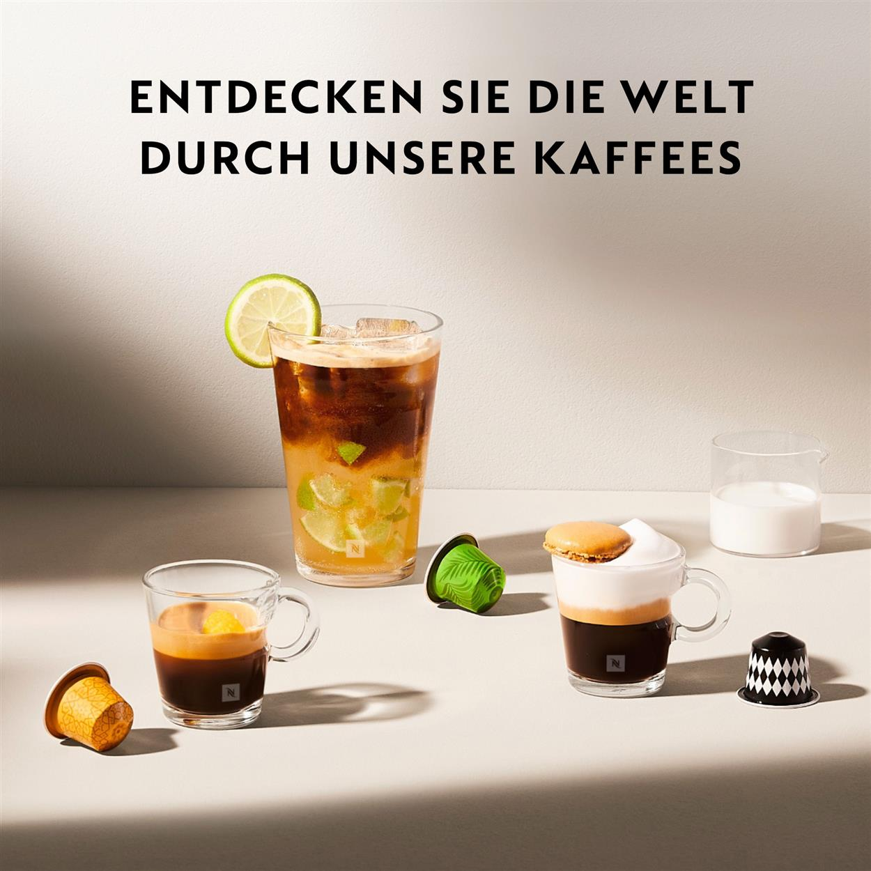 Kaffeegetränke in Gläsern. Auf dem Tisch befinden sich mehrere Kaffeetassen und -kapseln.