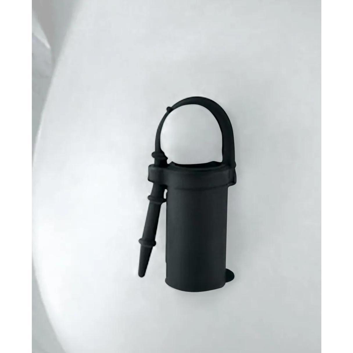 Ein schwarzer Halter für ein kleines Objekt. Er hat einen Schlaufengriff und einen Clip.