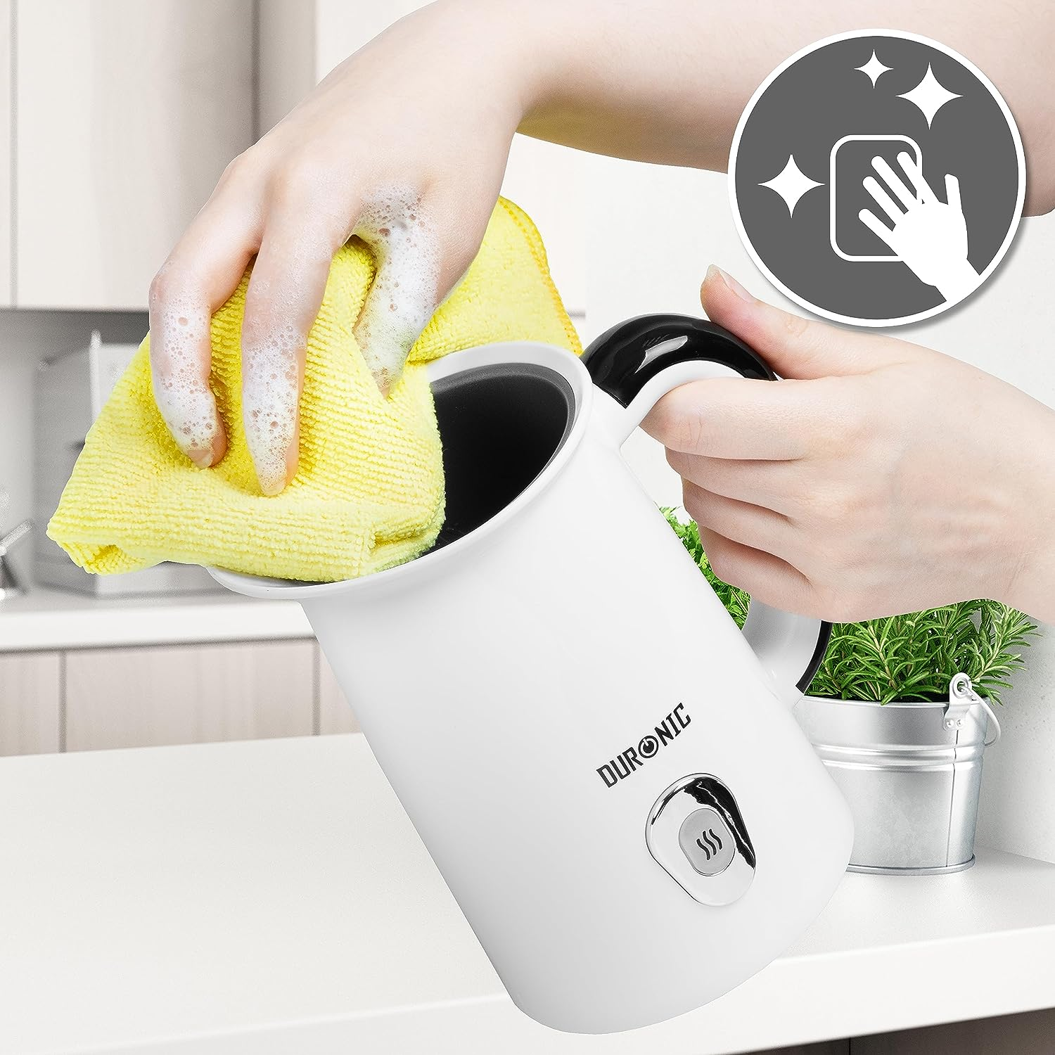 Eine Person reinigt einen weißen elektrischen Wasserkocher mit einem gelben Tuch und einem Seifenblasenbild.