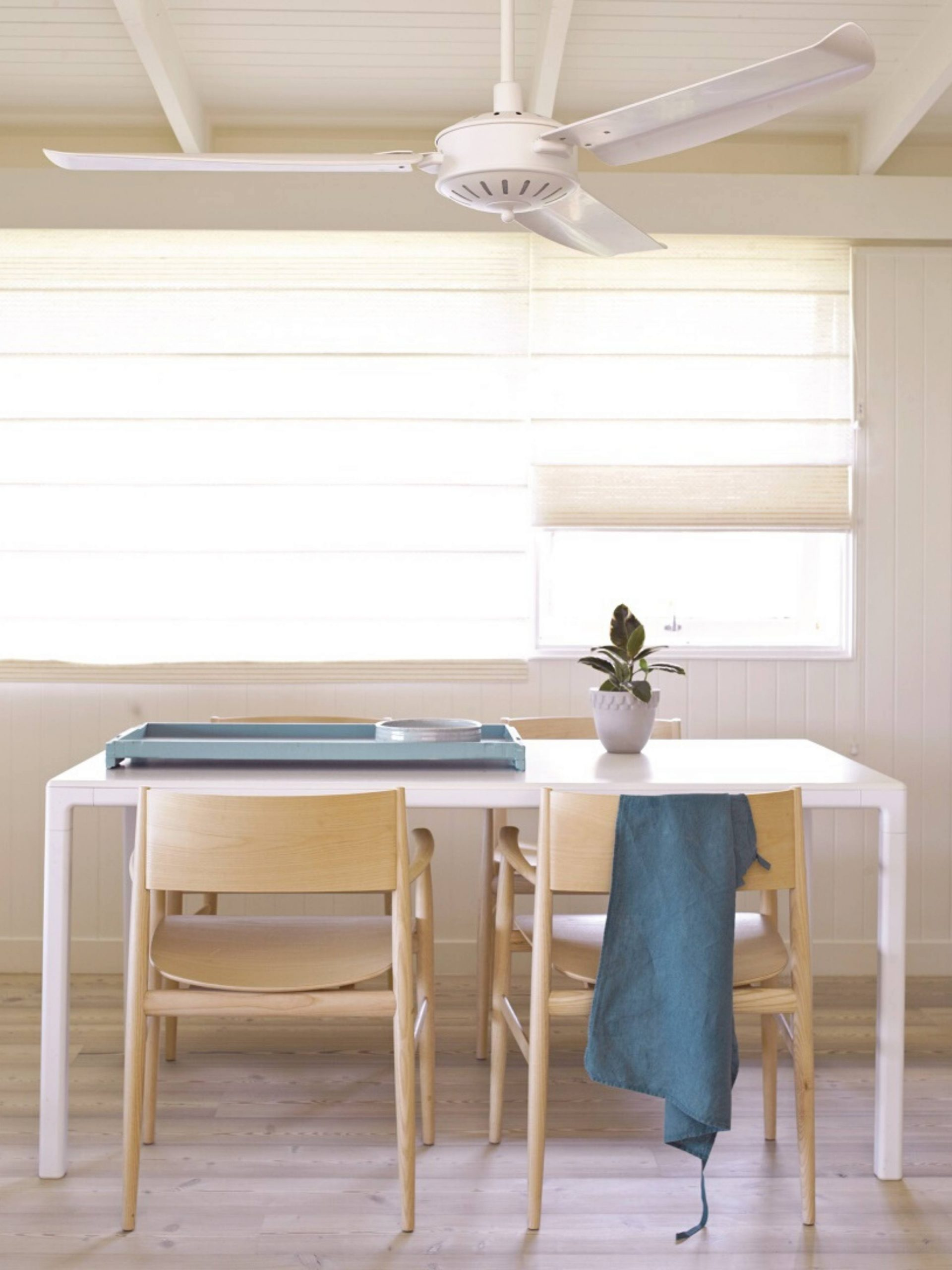Ein Esszimmer mit weißem Tisch, Holzstühlen und Deckenventilator. Blaues Tablett und Handtuch.