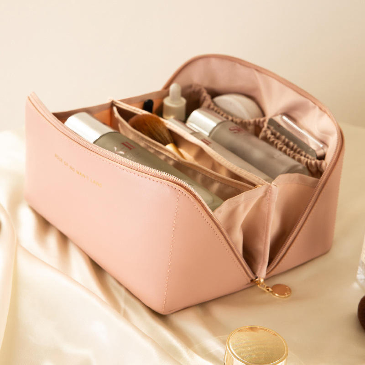 Offene rosa Make-up-Tasche mit Fächern, gefüllt mit Kosmetika. Auf einer Satin-Oberfläche platziert.