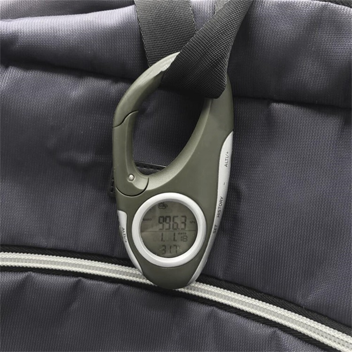 Grauer und schwarzer digitaler Höhenmesser an einem grauen Rucksack befestigt. Knöpfe und ein Bildschirm sind sichtbar.