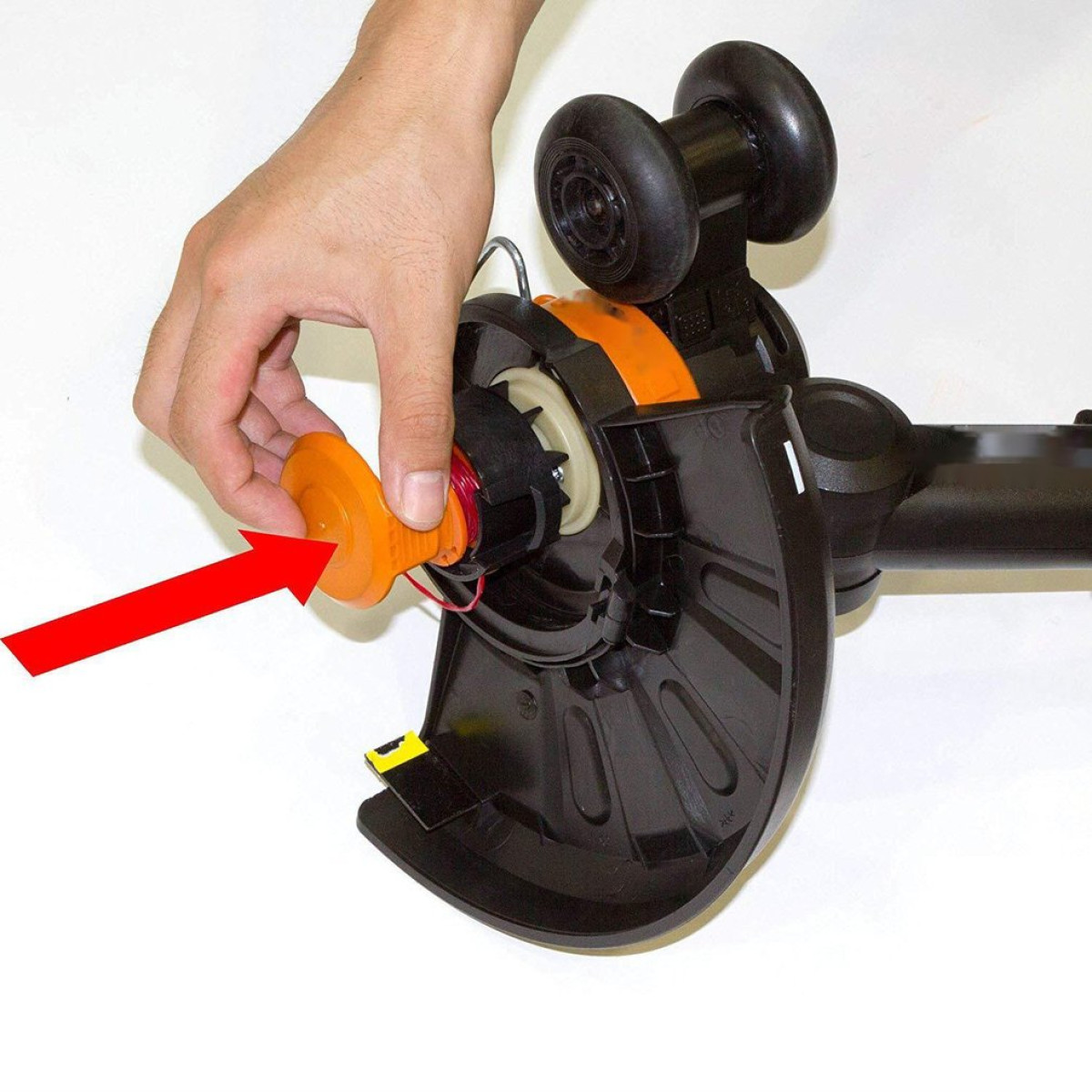 Een hand die naar een oranje spoel in een zwarte en oranje trimmer wijst.