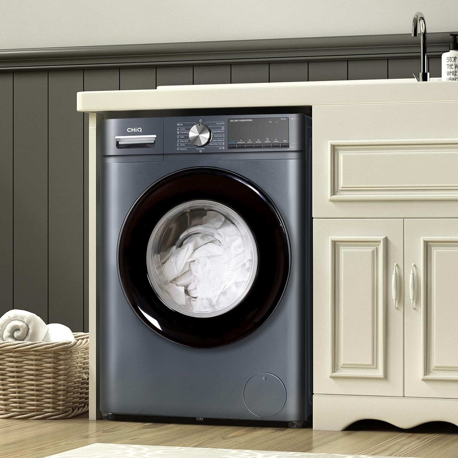 Lave-linge gris devant un meuble crème. Panier à linge à gauche.