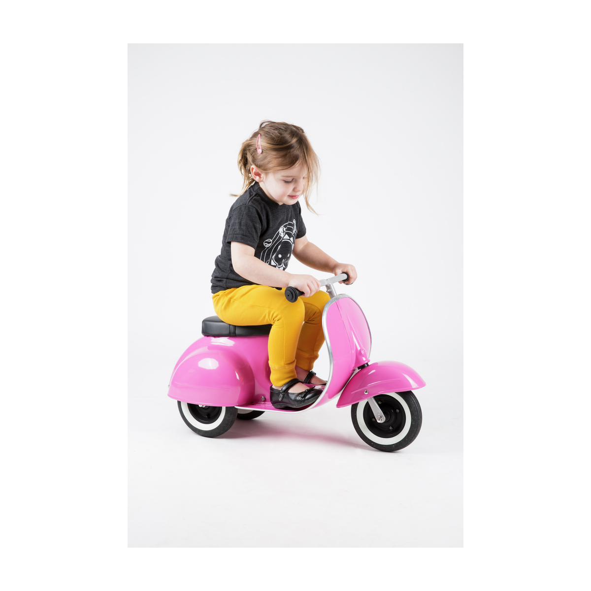 Un bambino che guida uno scooter rosa su sfondo bianco.