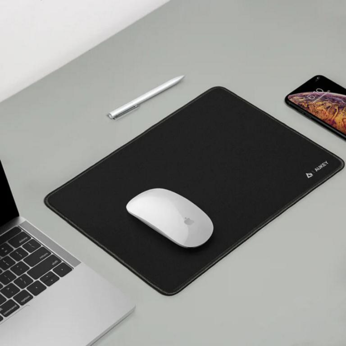 Eine schwarze Mauspads mit einer weißen Maus, Stift und Telefon auf einem grauen Schreibtisch.