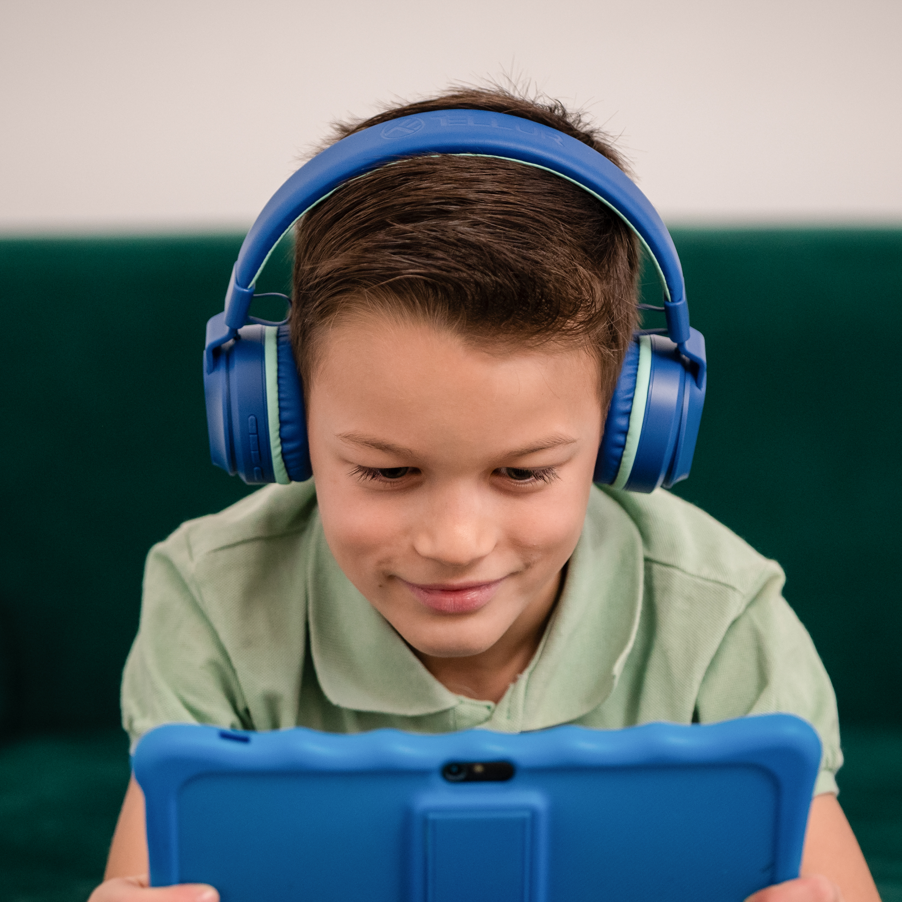 Chłopiec w niebieskich słuchawkach patrzący na tablet z niebieskim etui.