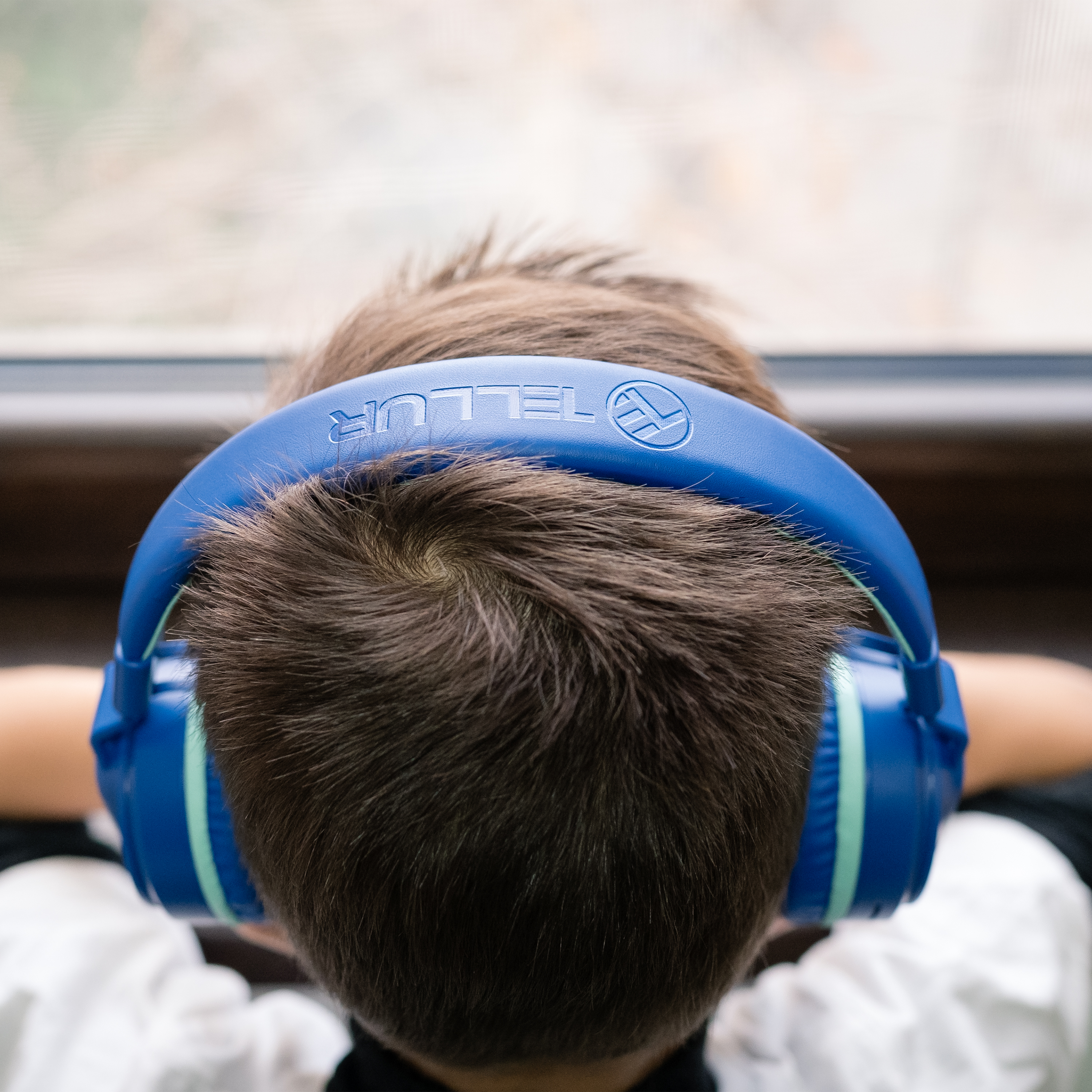 Chłopiec widziany od tyłu, w niebieskich słuchawkach, patrzący na okno.
