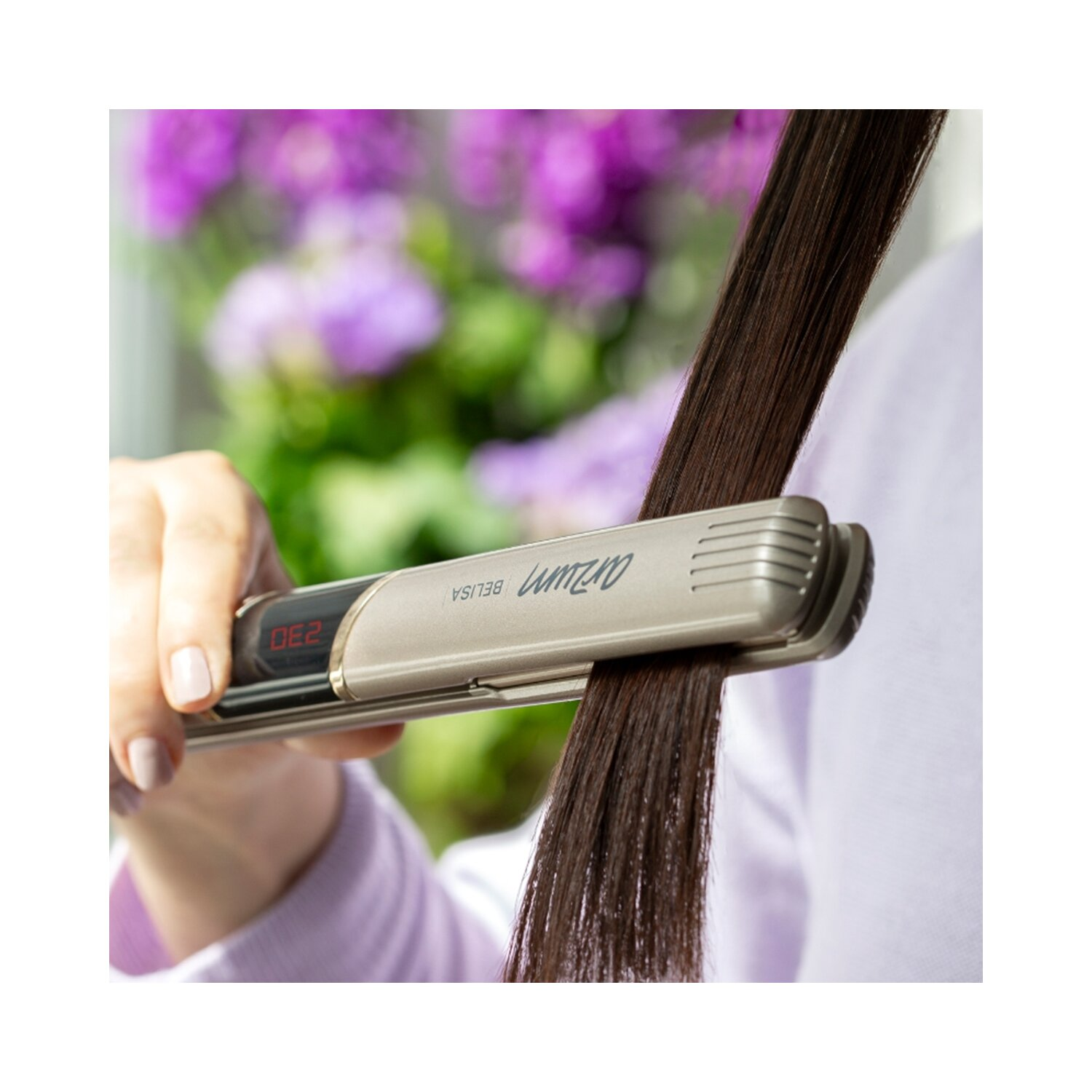 Eine Frau benutzt einen Haarglätter auf einer langen Haarsträhne. Der Hintergrund ist verschwommen.