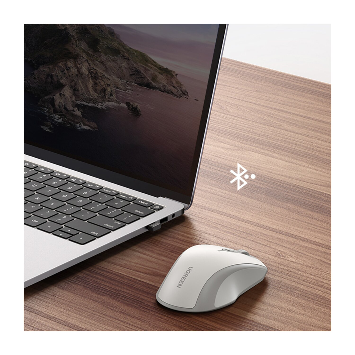 Biała mysz UGREEN obok otwartego laptopa na drewnianym biurku z ikoną Bluetooth.
